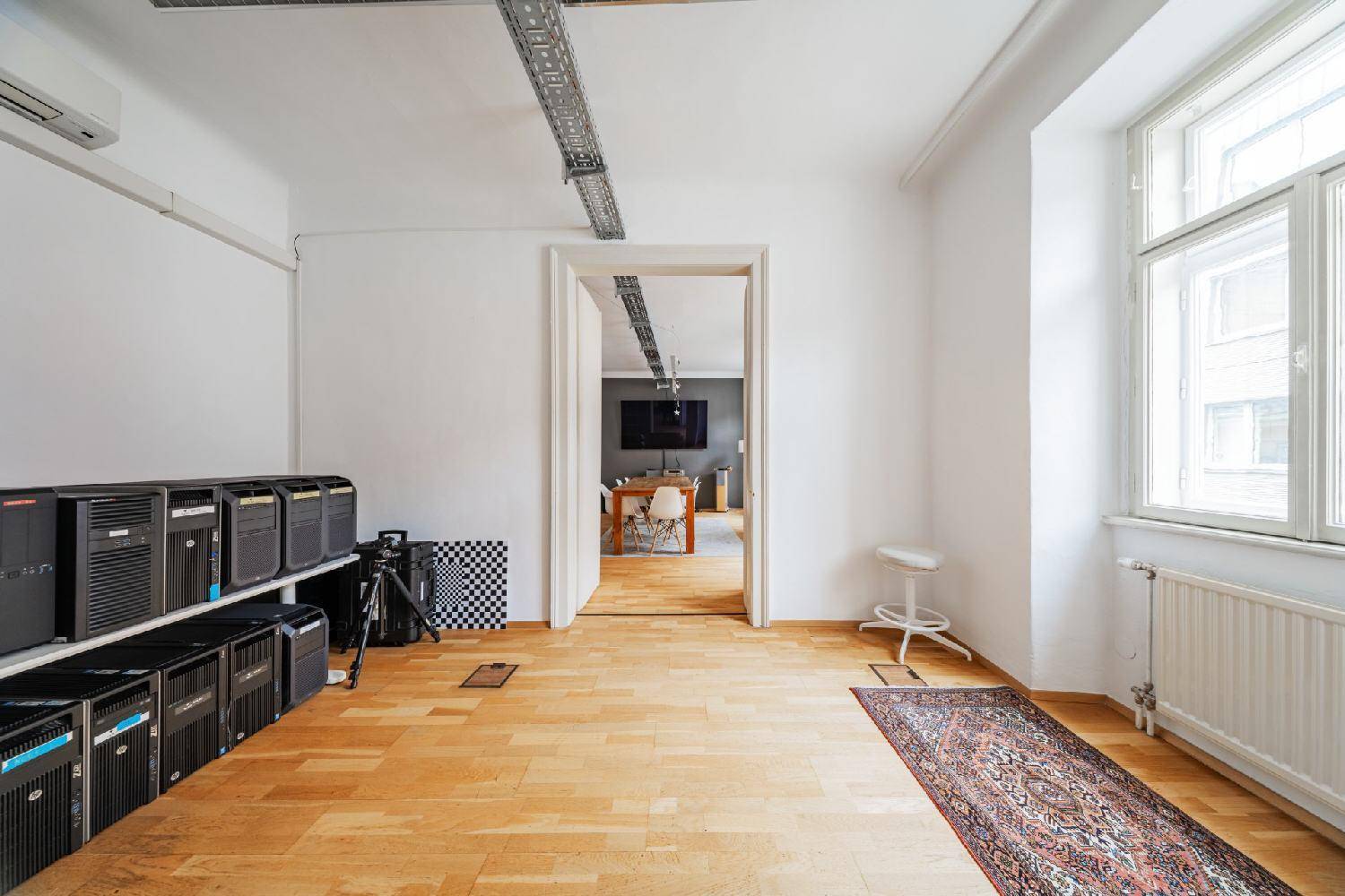 Geräumiger Büroraum mit Holzboden, Server-Racks und einem Fenster, das Tageslicht hereinlässt.