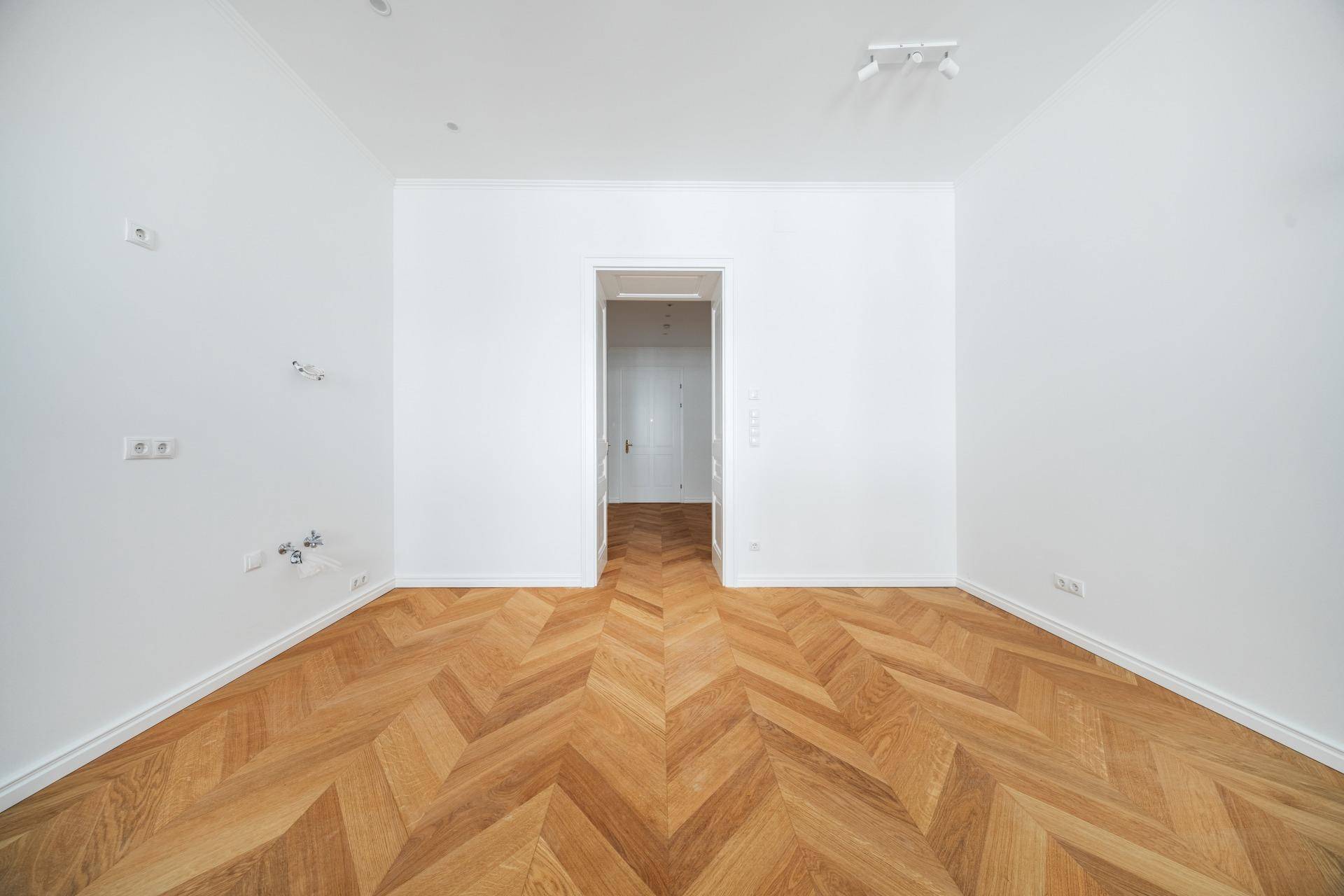 Heller Raum mit Fischgrätparkett und einem Durchgang zu einem weiteren Zimmer.