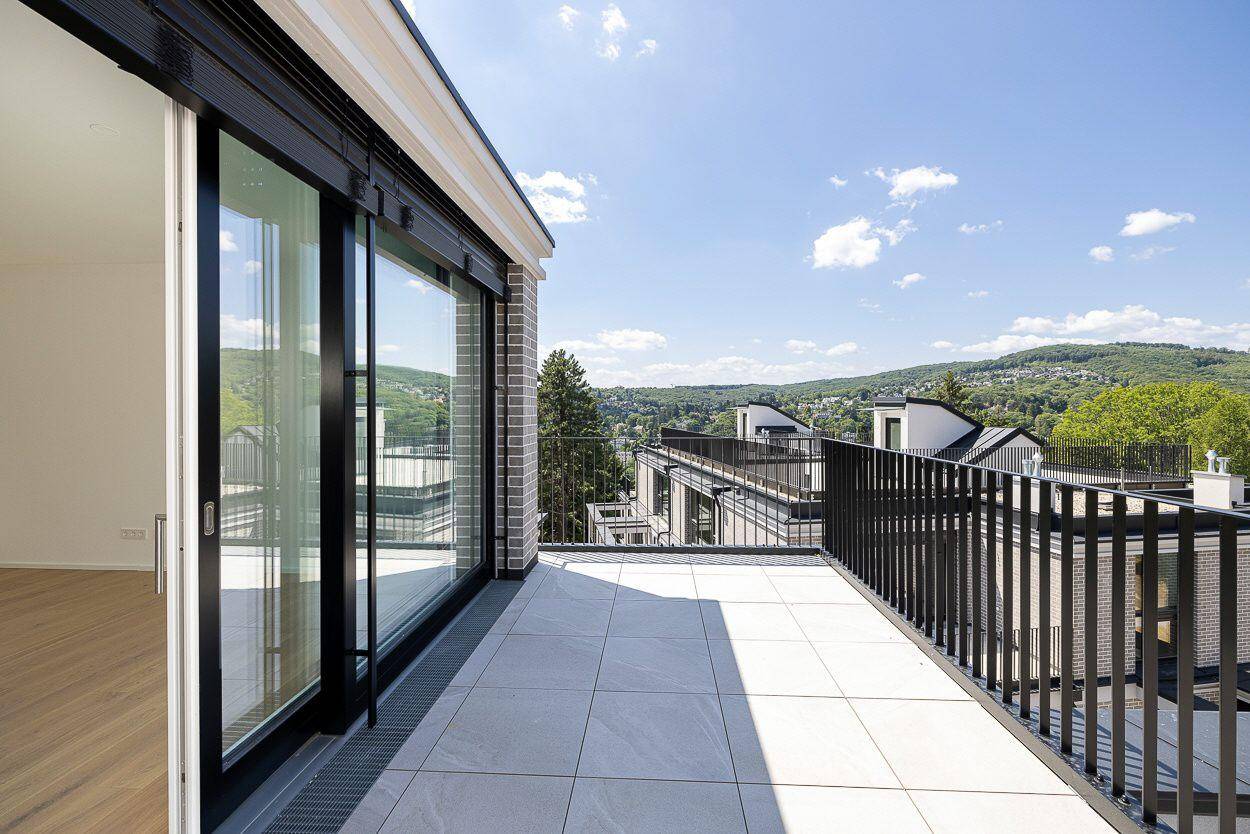 Große Terrasse mit Fliesenboden und schwarzem Geländer, bietet einen Panoramablick ins Grüne.