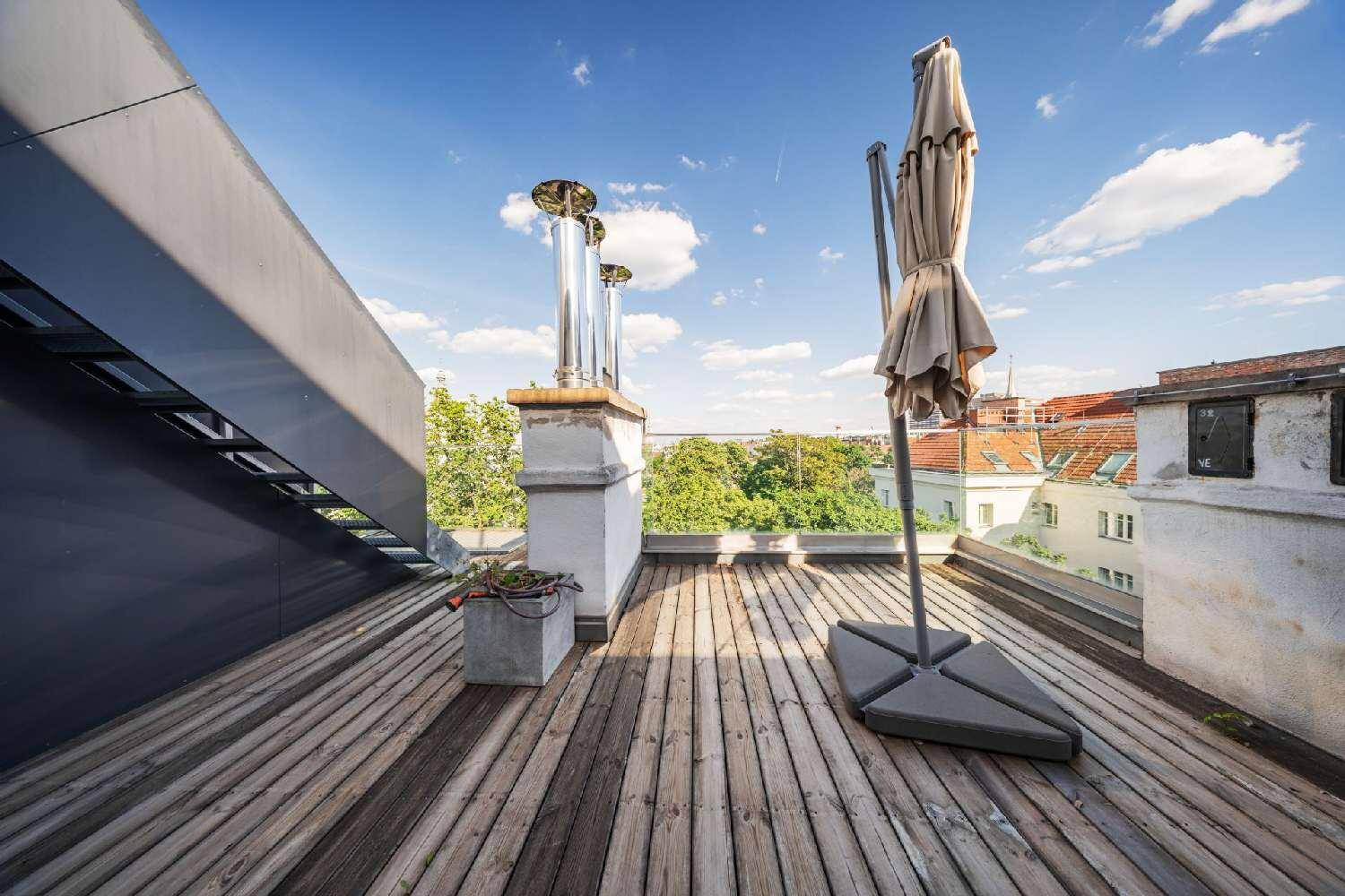 Teil der Dachterrasse mit Holzboden, Sonnenschirm und Blick auf die umliegenden Bäume.