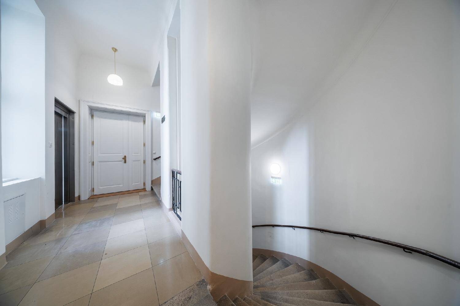 Heller Flur mit weiß gestrichenen Wänden, gefliestem Boden und einer eleganten Wendeltreppe.