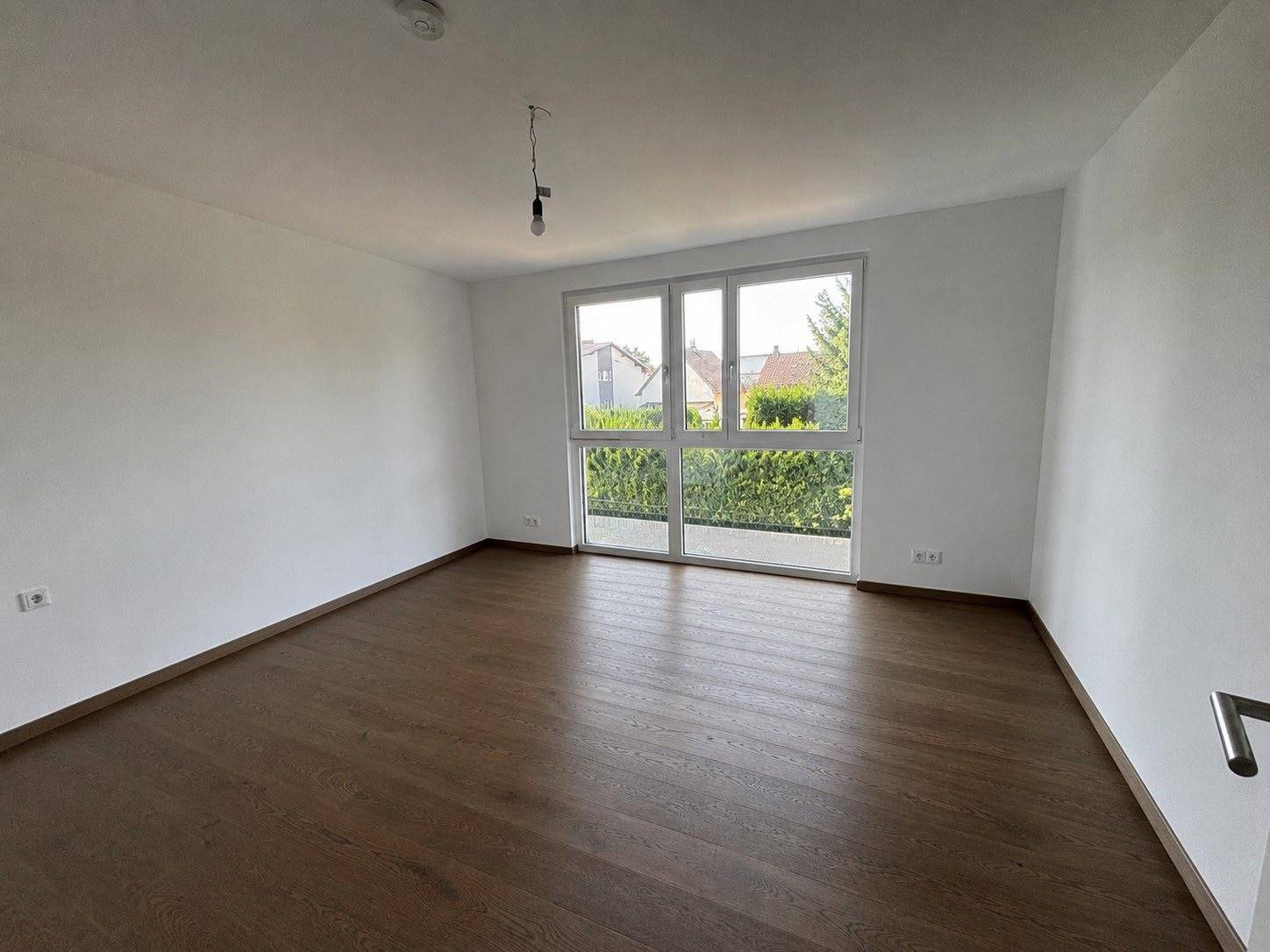Helles Zimmer mit Holzboden und großen Fenstern mit Blick ins Grüne.