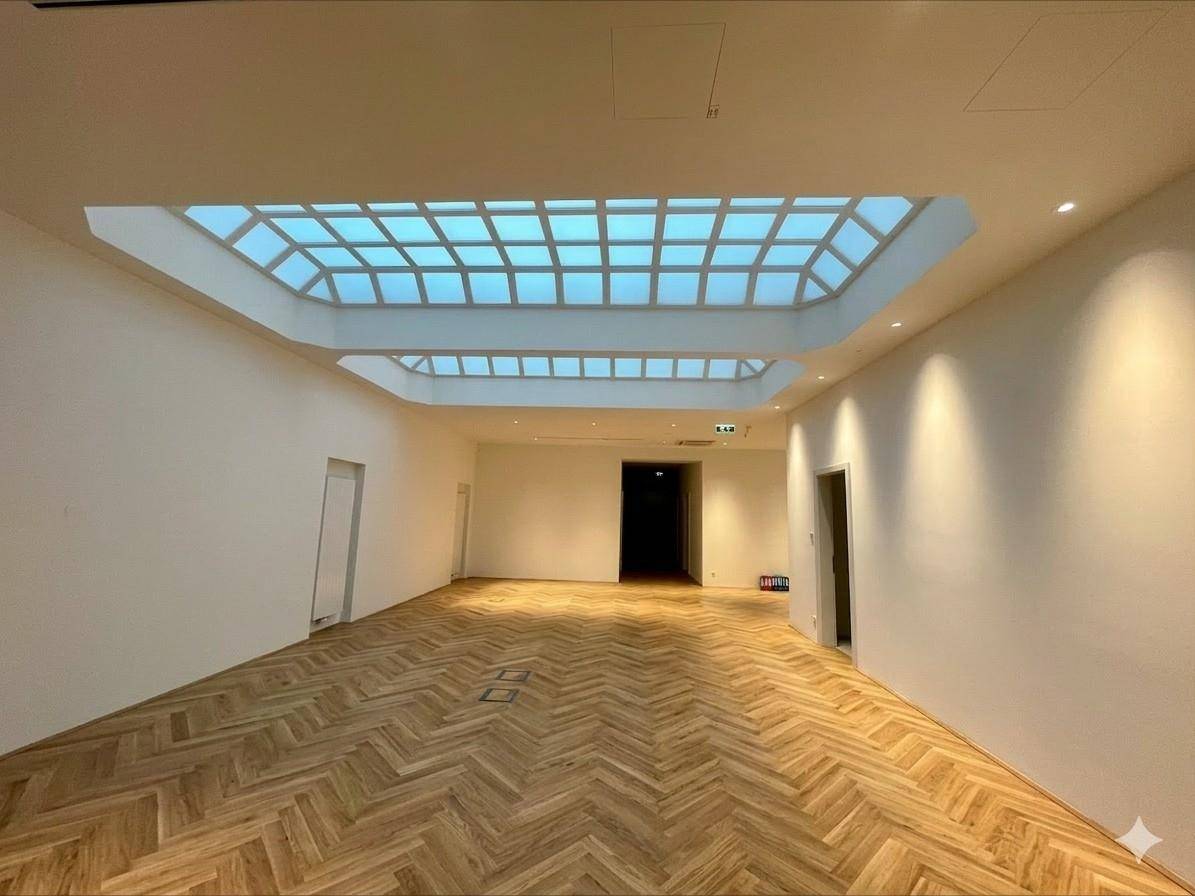 Großer, heller Raum mit Fischgrätparkett und zwei markanten Oberlichtern, die viel Tageslicht hereinlassen.