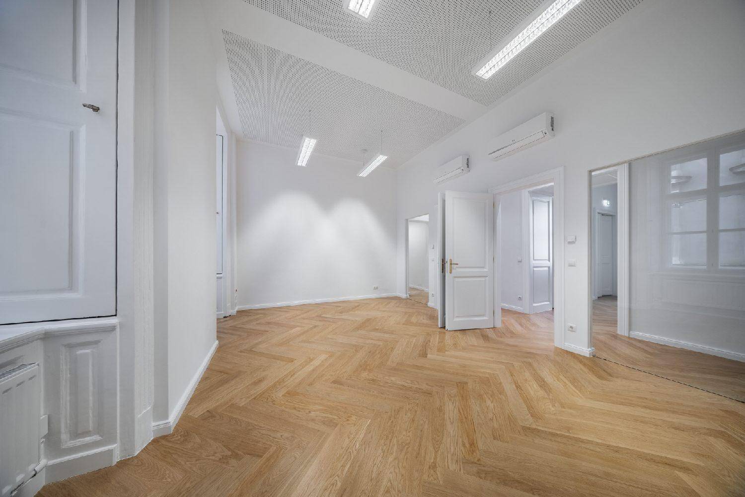 Heller, leerer Raum mit Fischgrätparkett, Klimaanlage und einem großen Spiegel an der Wand.