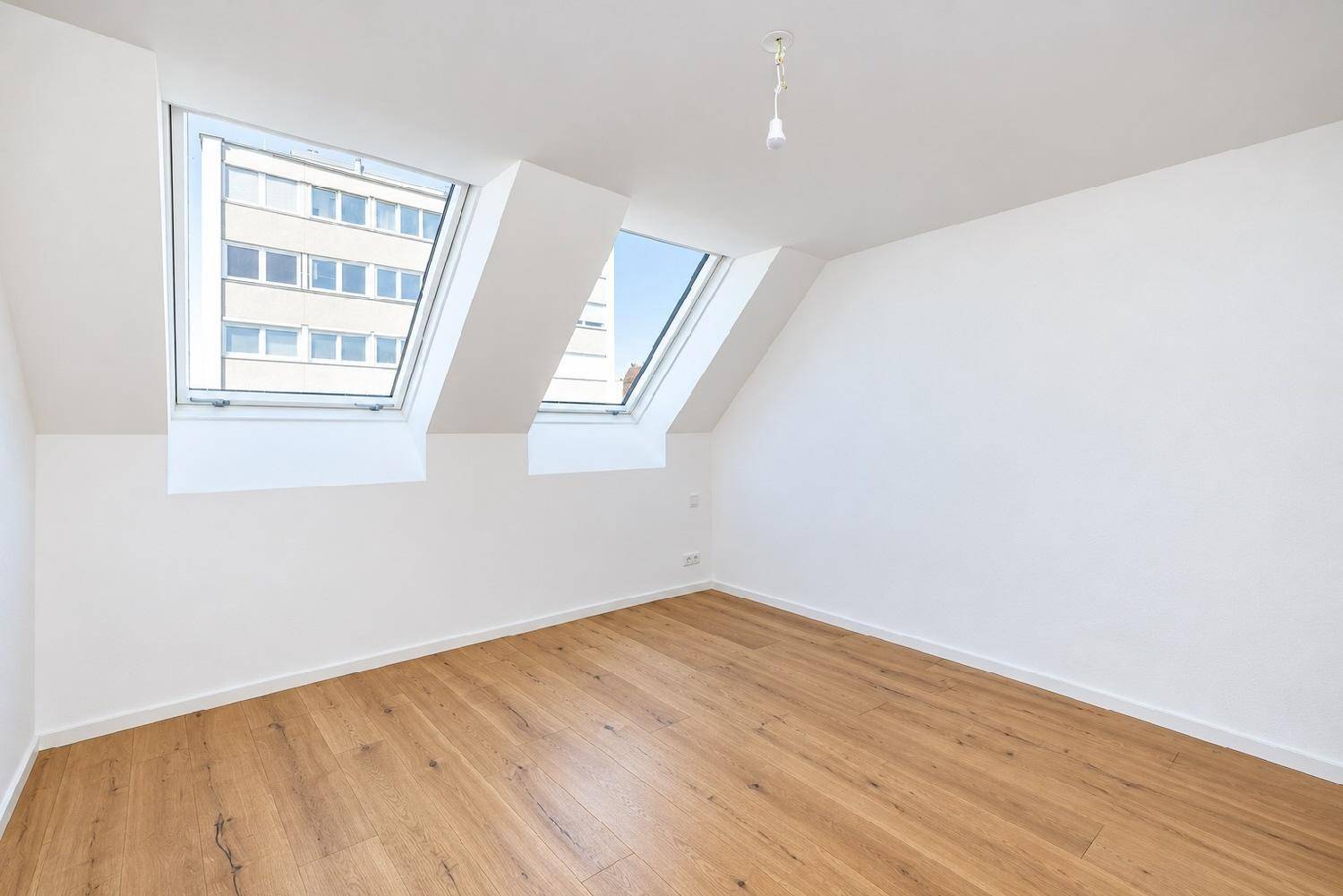 Helles Schlafzimmer im Dachgeschoss mit Holzboden und zwei großen Dachfenstern, bietet viel Tageslicht.