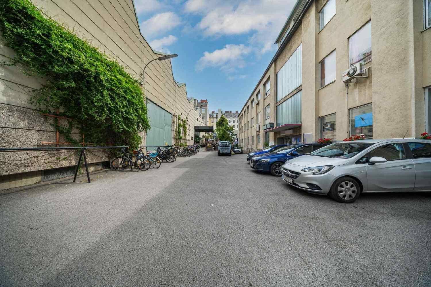 Außenansicht eines Gebäudes mit Parkplätzen und Fahrrädern im Hofbereich, zeigt die Zufahrt und Fassade.