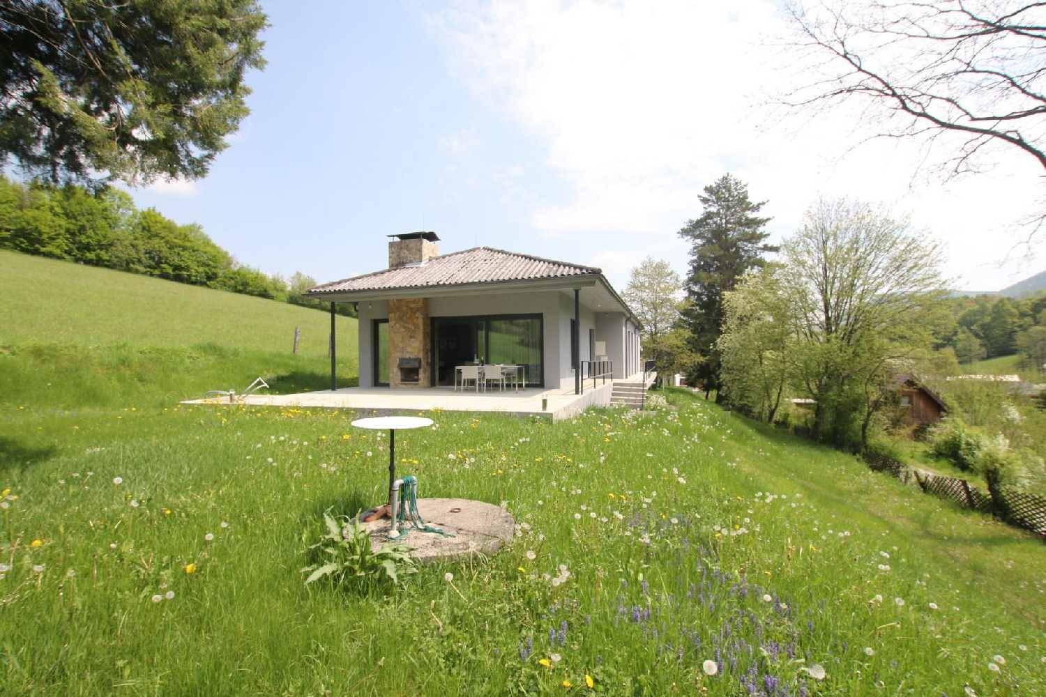 Modernes Einfamilienhaus in ländlicher Umgebung mit weitläufiger Grünfläche und Hügeln.