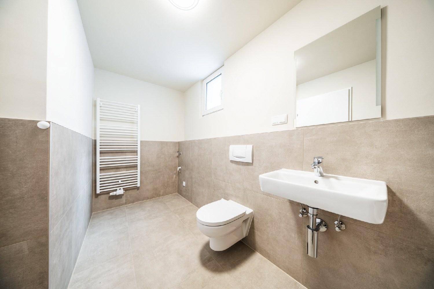 Modernes Badezimmer mit WC, Waschbecken, beheiztem Handtuchhalter und einem kleinen Fenster.