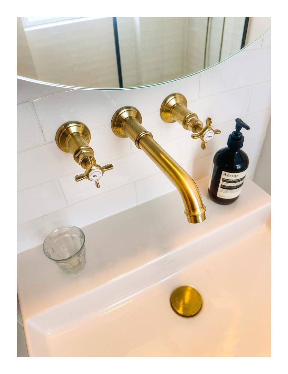 Detailaufnahme des Waschbeckens mit eleganten goldenen Armaturen und weißer Fliesenwand.