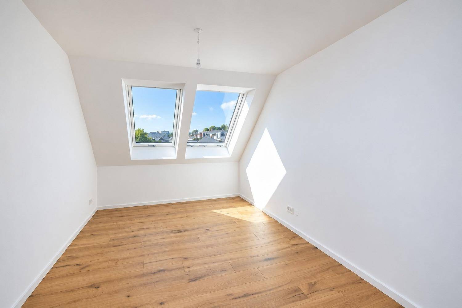 Schlafzimmer im Dachgeschoss mit Holzboden und zwei schrägen Dachfenstern für viel Licht.