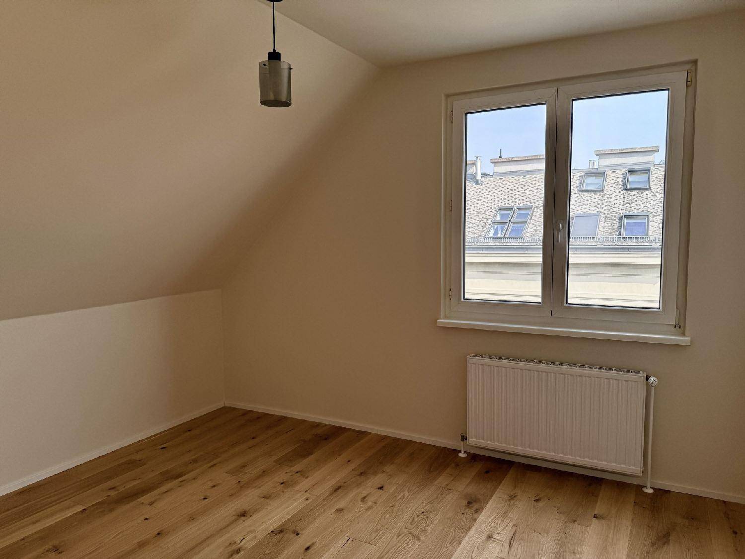 Helles Schlafzimmer mit Holzboden, Dachschräge und Blick auf umliegende Dächer.