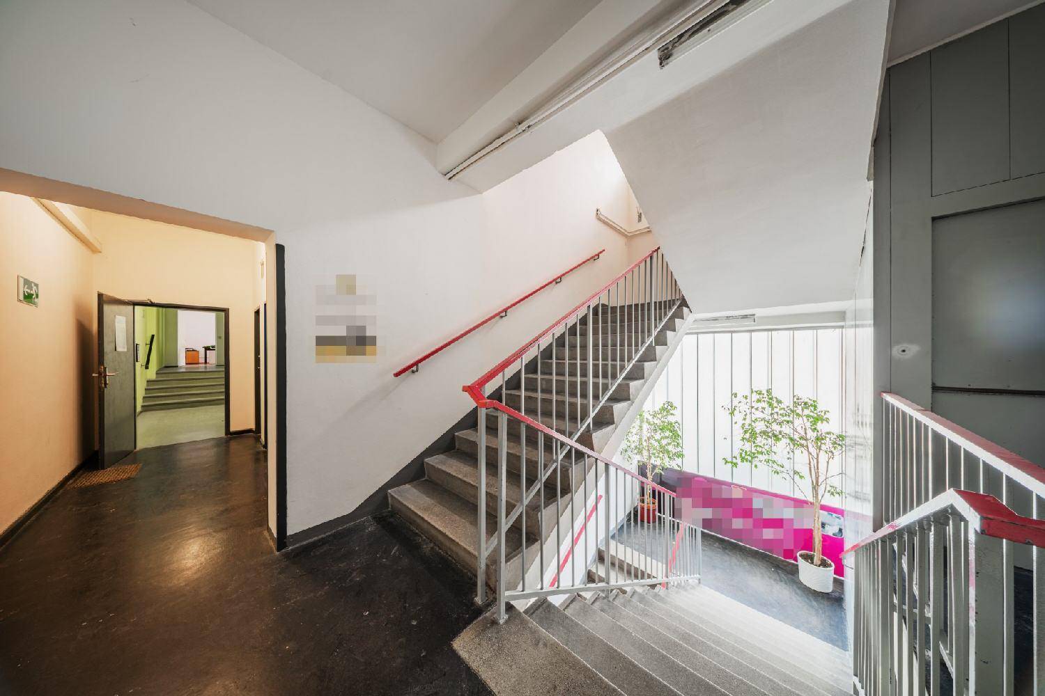 Geräumiges Treppenhaus mit Betonstufen, roten Handläufen und viel Tageslicht, verbindet die Etagen effizient.