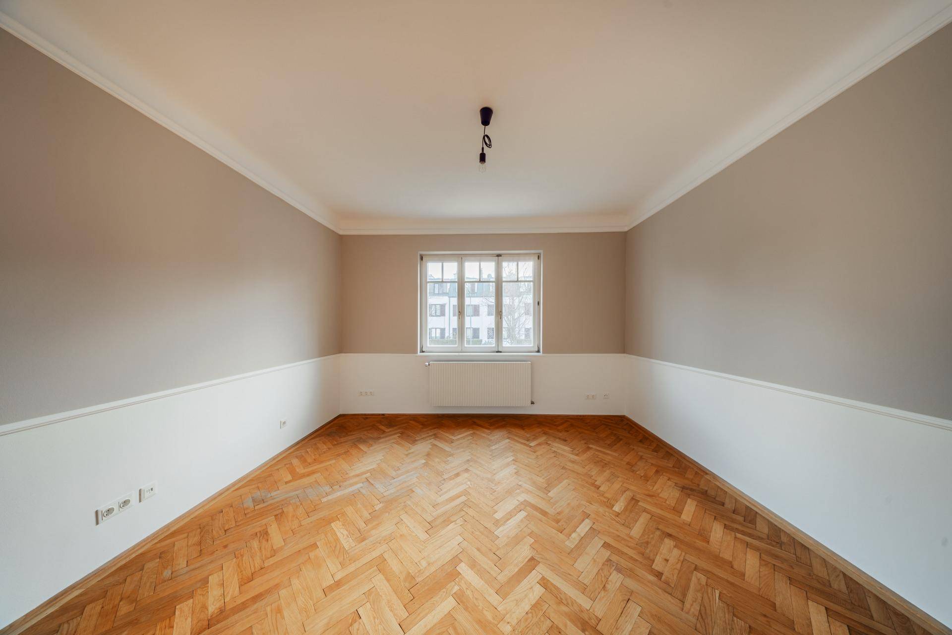 Helles Schlafzimmer mit Fischgrätparkett, neutralen Wänden und einem großen Fenster für Tageslicht.