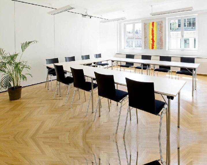 Heller Konferenzraum mit U-förmiger Tischordnung, Holzparkettboden und großen Fenstern mit Stadtblick.