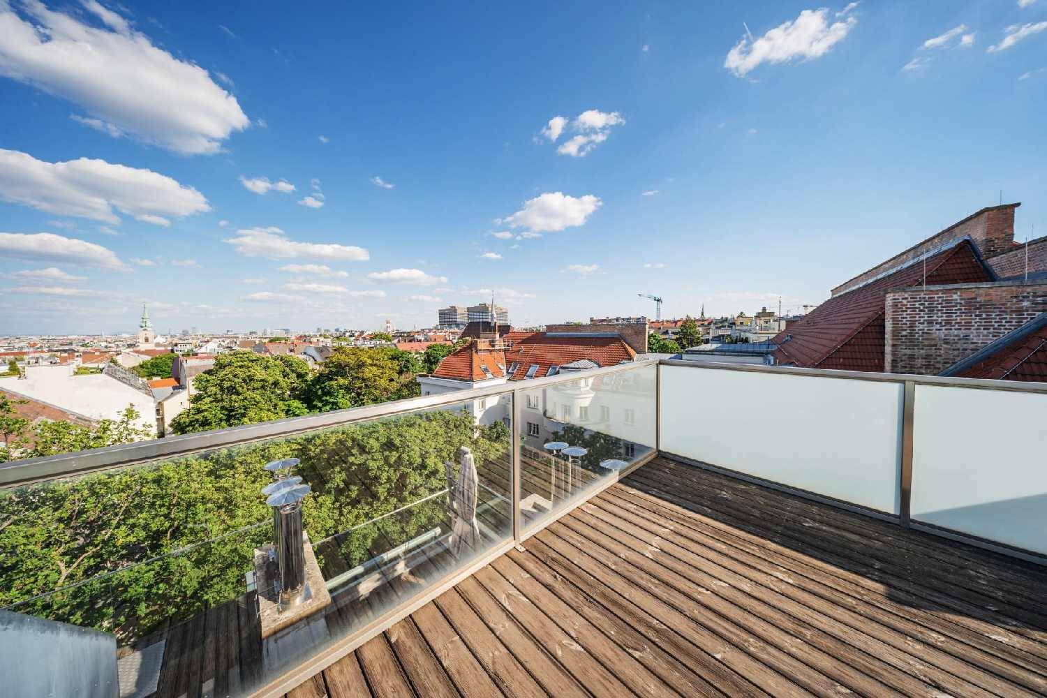 Dachterrasse mit Holzboden und modernem Glasgeländer, das einen weiten Blick über die Stadt ermöglicht.