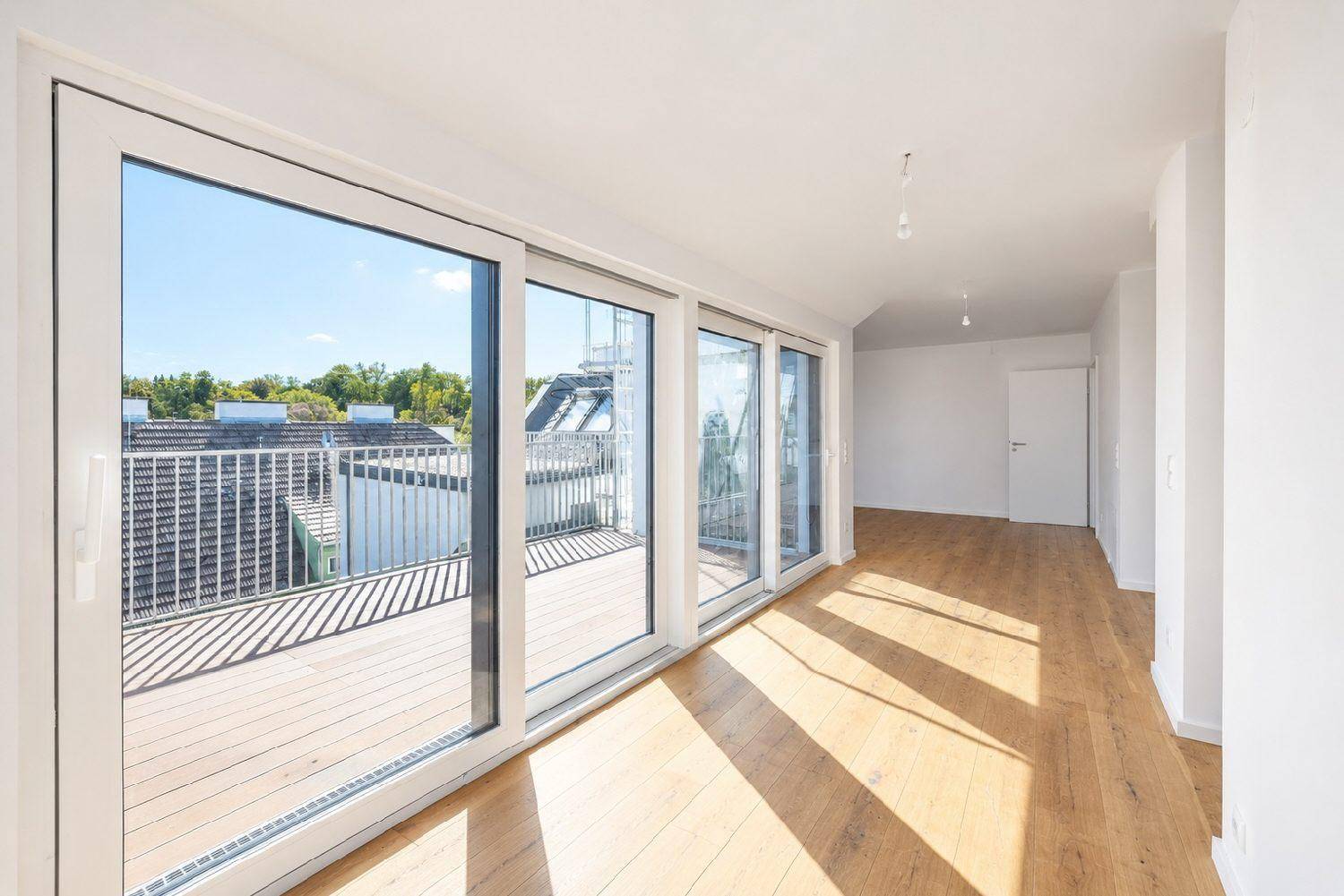 Lichtdurchfluteter Wohnbereich mit Holzboden und großen Fenstern, die auf eine sonnige Dachterrasse führen.
