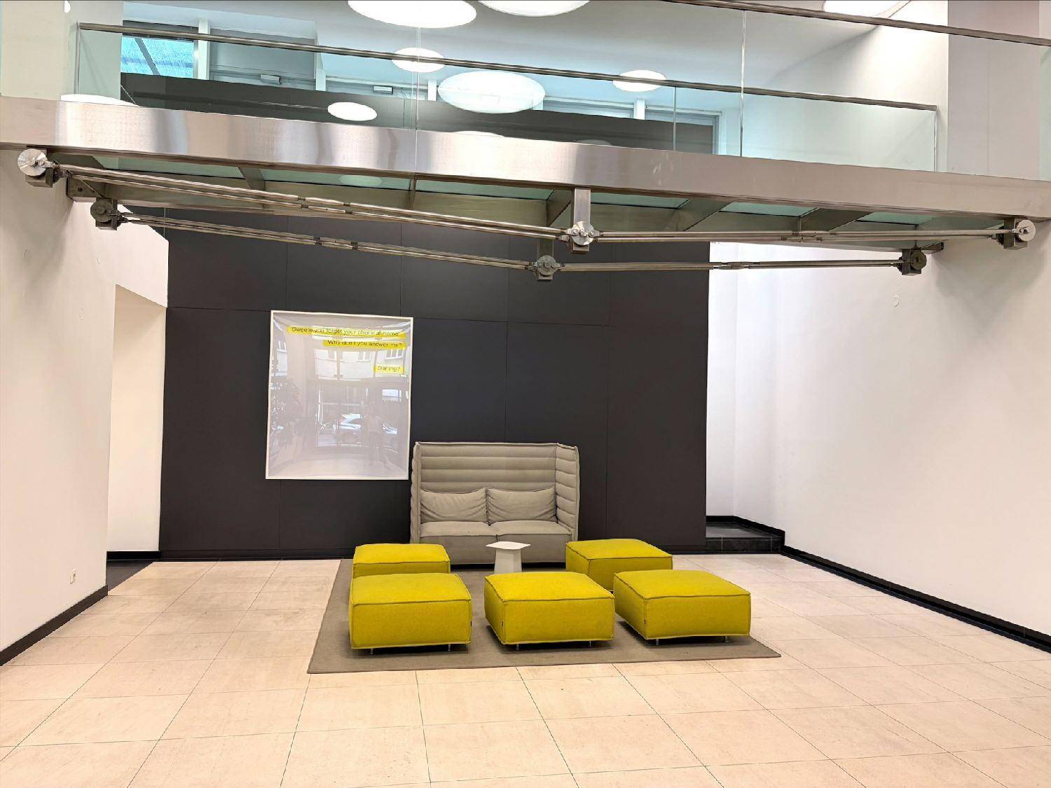 Moderner Empfangsbereich mit beigem Sofa, gelben Hockern und einer Galerie mit Glasgeländer.