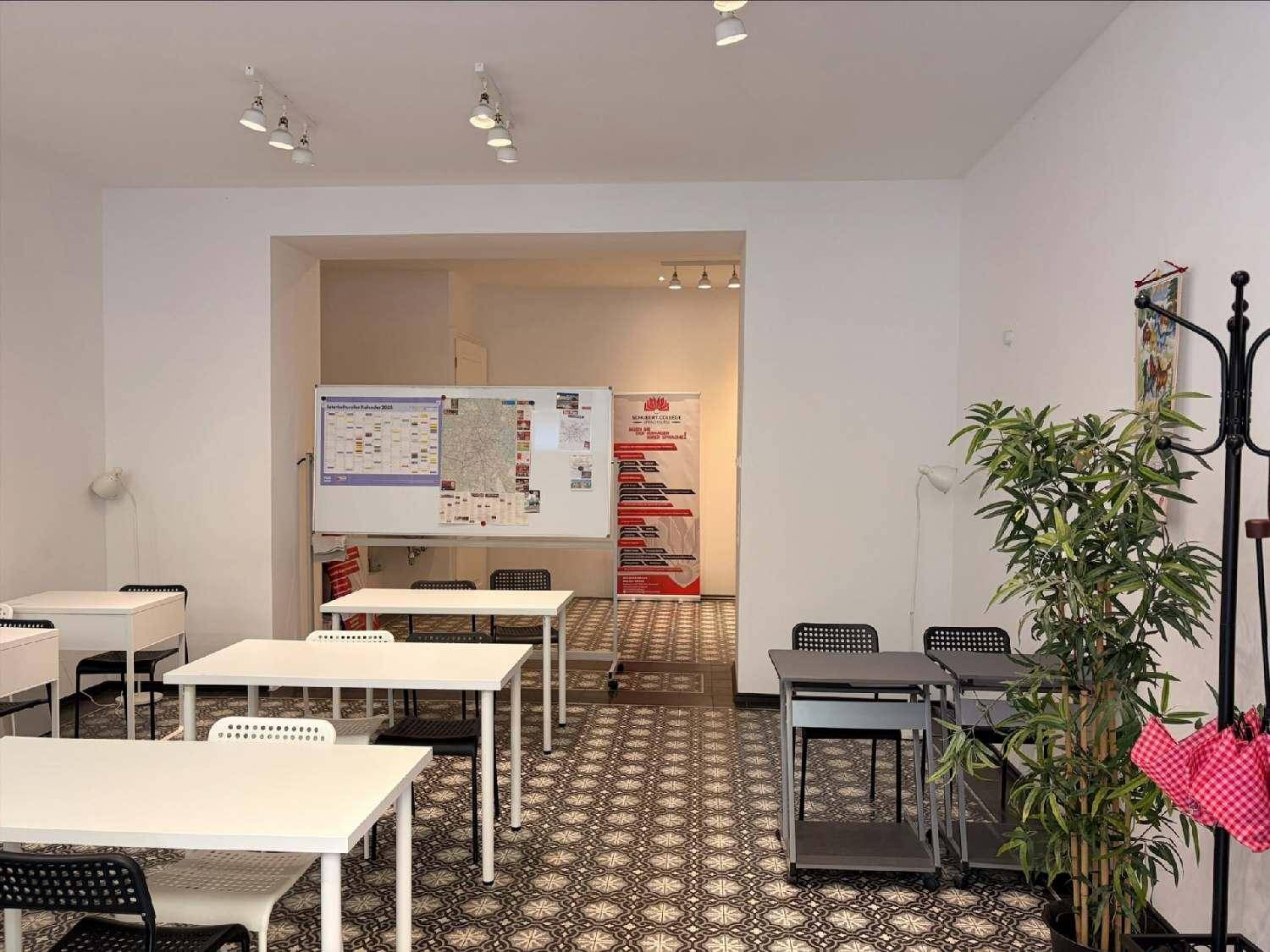 Übersicht des Klassenraums mit Tischen, Stühlen und einer Whiteboard-Tafel, die zu einem weiteren Bereich führt.