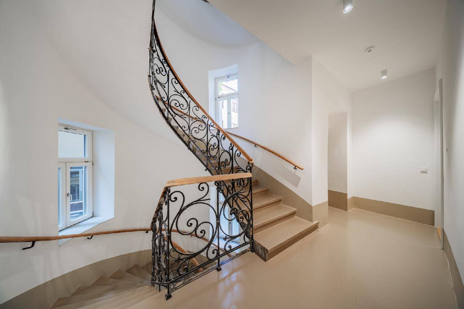 Elegantes Treppenhaus mit geschwungenem schmiedeeisernem Geländer und Holzhandlauf.