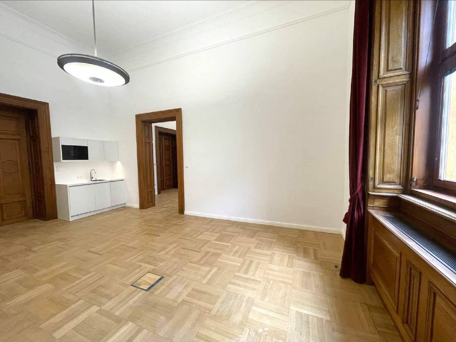 Geräumiger Raum mit Fischgrätparkett, hohen Decken und einer modernen Küchenzeile neben einem großen Fenster.