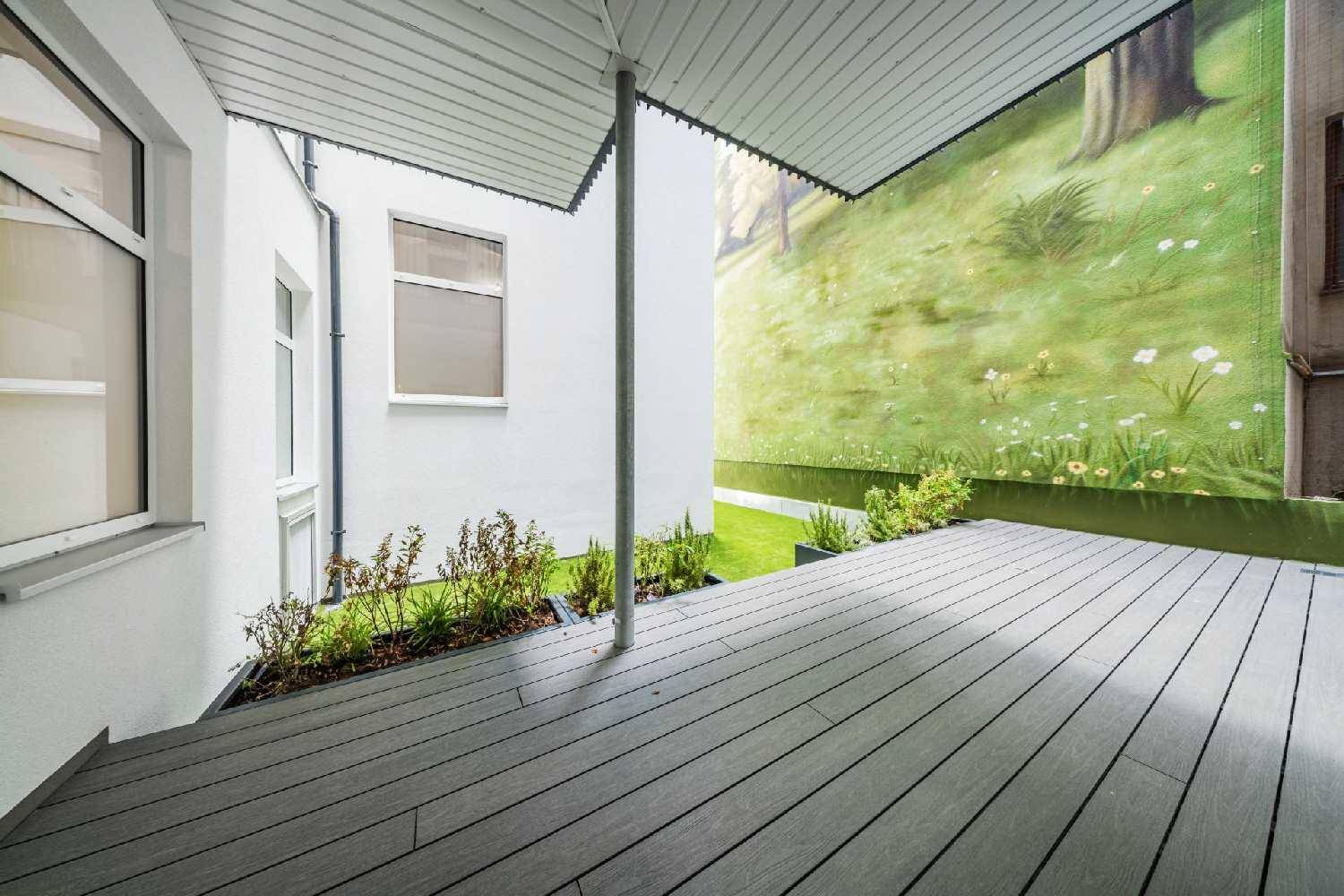 Moderne Terrasse mit grauen Dielen, Pflanzenbeeten und einer grünen Wandmalerei für eine angenehme Atmosphäre.