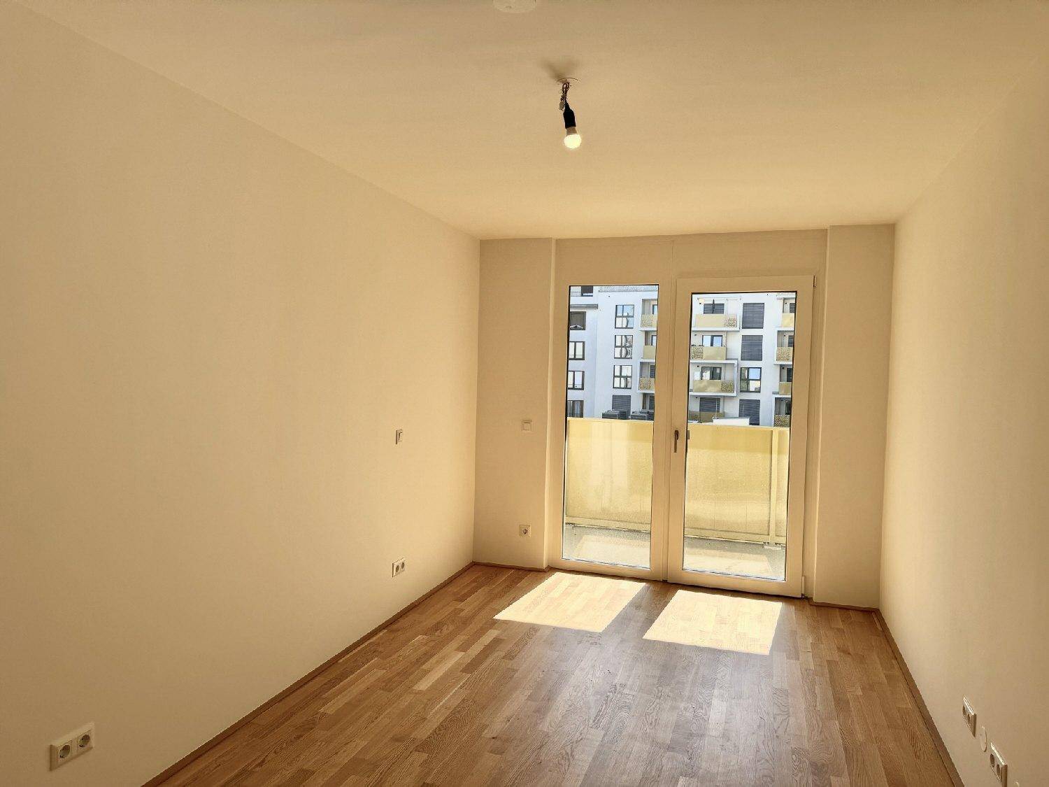 Lichtdurchfluteter Raum mit Parkettboden und Balkonzugang, ideal für ein Wohn- oder Schlafzimmer.