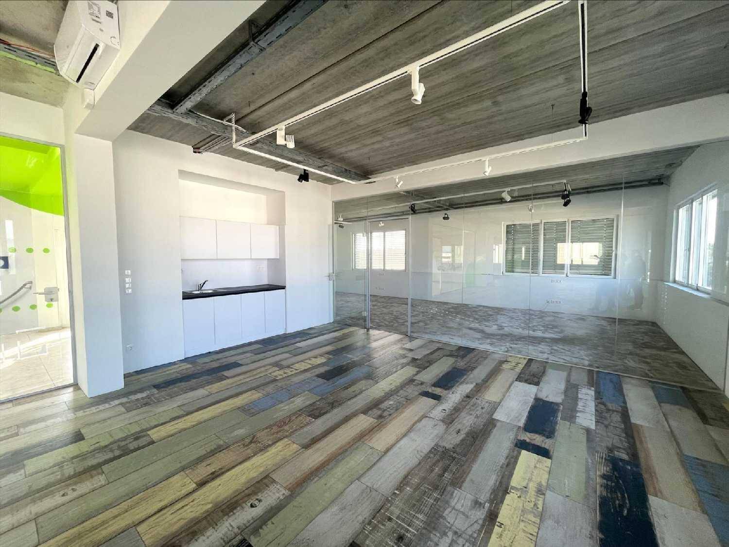 Modernes Büro mit kleiner Küchenzeile, Glaswänden und farbigem Holzboden.