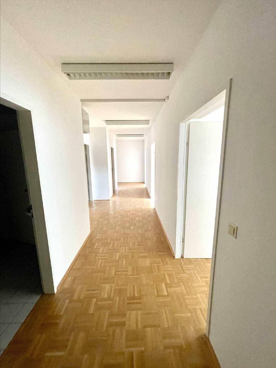 Langer, heller Flur mit Parkettboden und mehreren Türen, der verschiedene Büros verbindet und gut beleuchtet ist.
