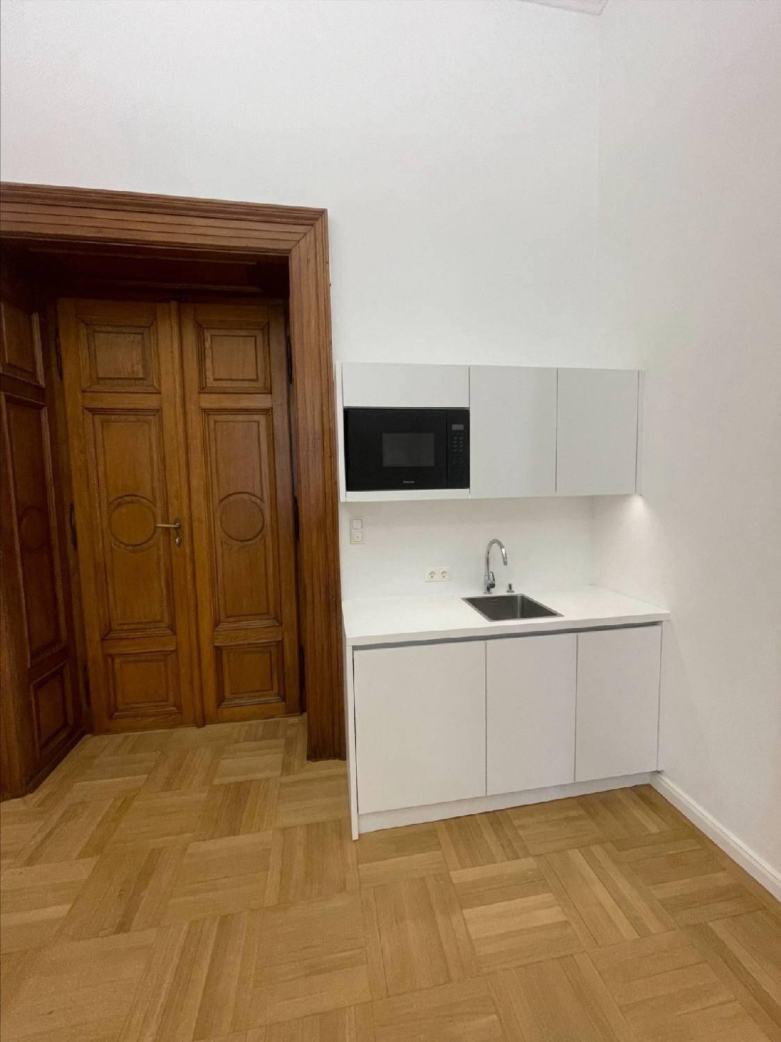 Detailansicht einer modernen, weißen Küchenzeile mit Spüle und integrierter Mikrowelle neben einer klassischen Holztür.