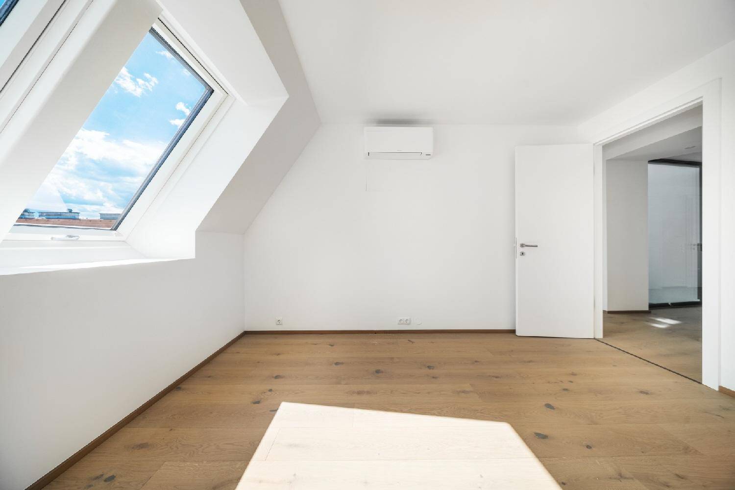 Geräumiges Zimmer mit Holzboden, großem Dachfenster und Klimaanlage, ideal als Schlafzimmer.