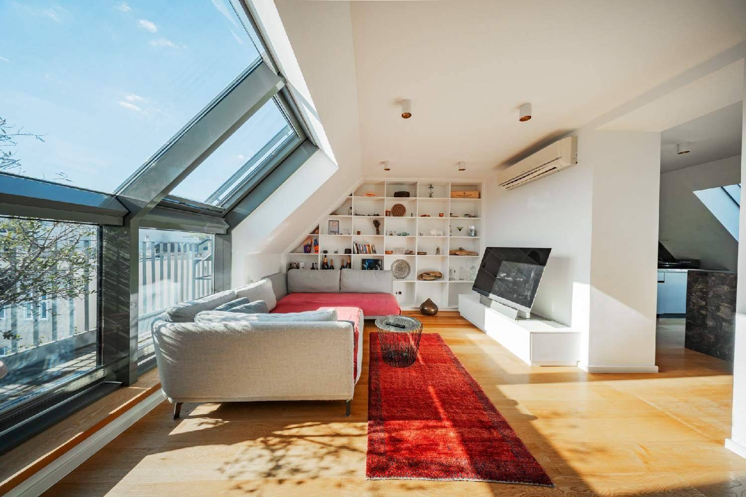 Helles Wohnzimmer mit großen Dachfenstern, Holzboden und integrierten Regalen.