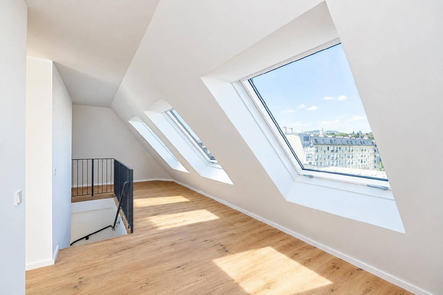 Lichtdurchfluteter Dachgeschossbereich mit Holzfußboden und Treppenabgang, bietet einen weiten Stadtblick.