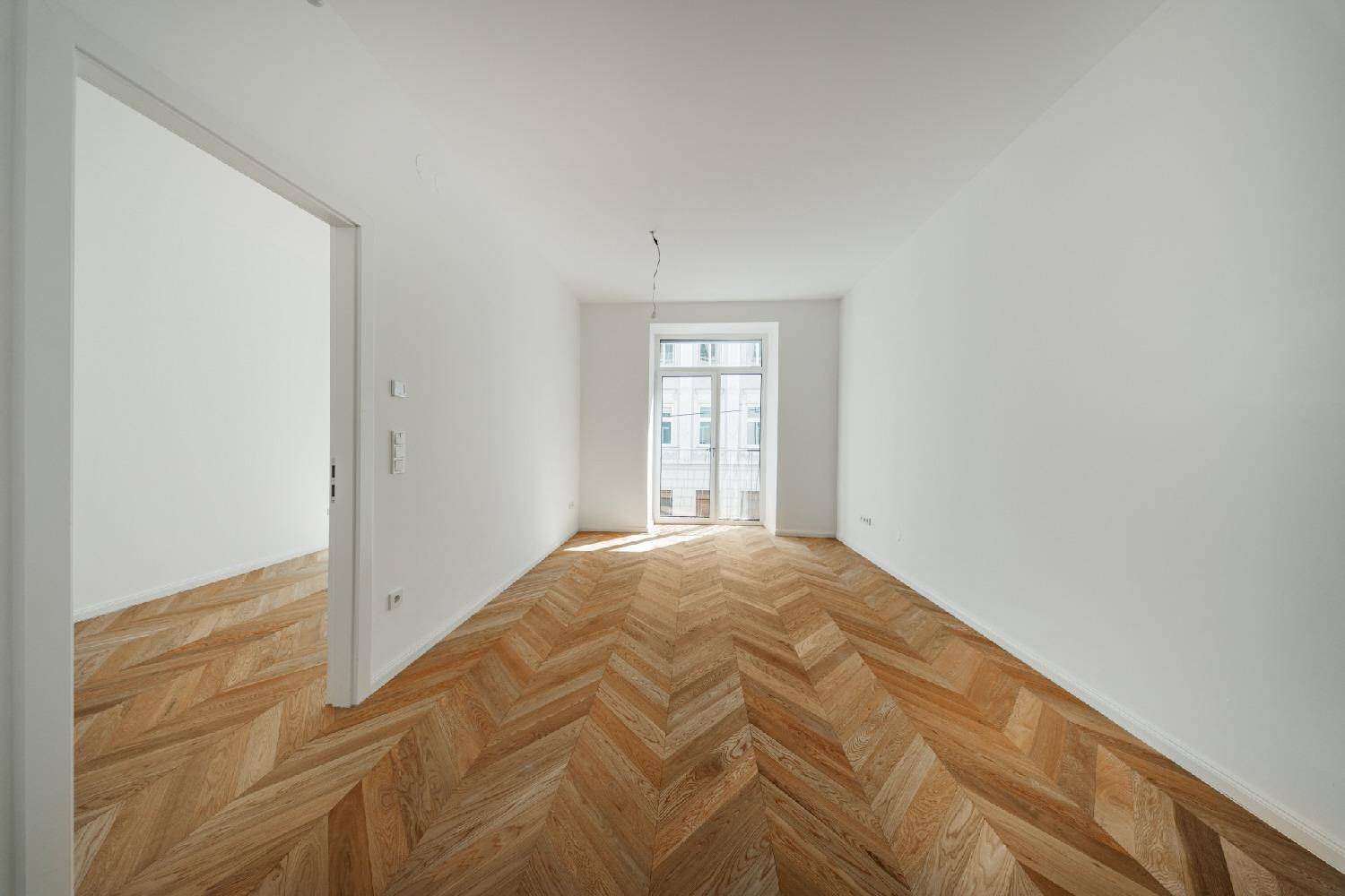 Unmöblierter Raum mit klassischem Fischgrätparkett und viel natürlichem Licht durch das Fenster.