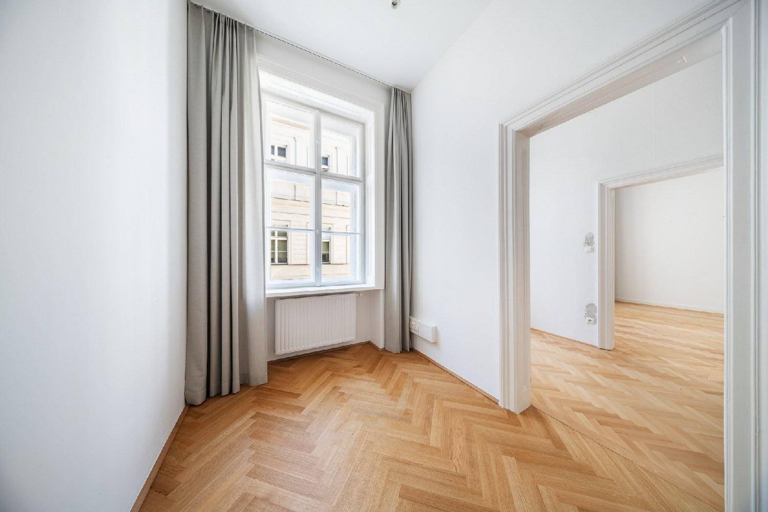 Kleiner Büroraum mit Fischgrätparkett, einem Fenster und Zugang zu anderen Zimmern.