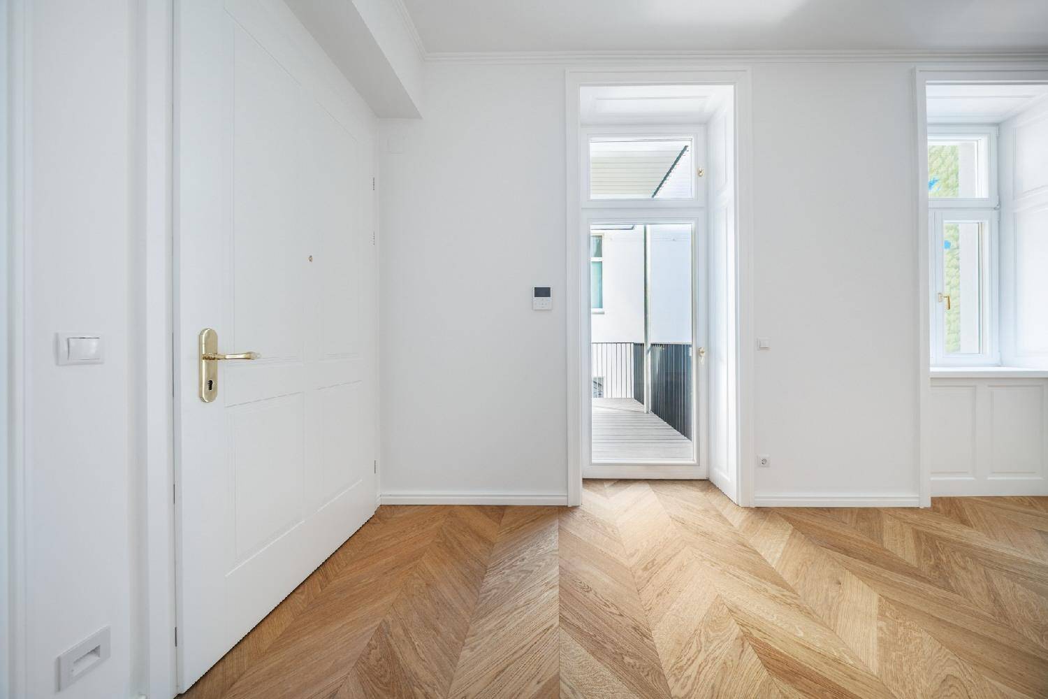 Heller Flur mit Fischgrätparkett und Zugang zu einem Balkon, bietet einen freundlichen Empfang.