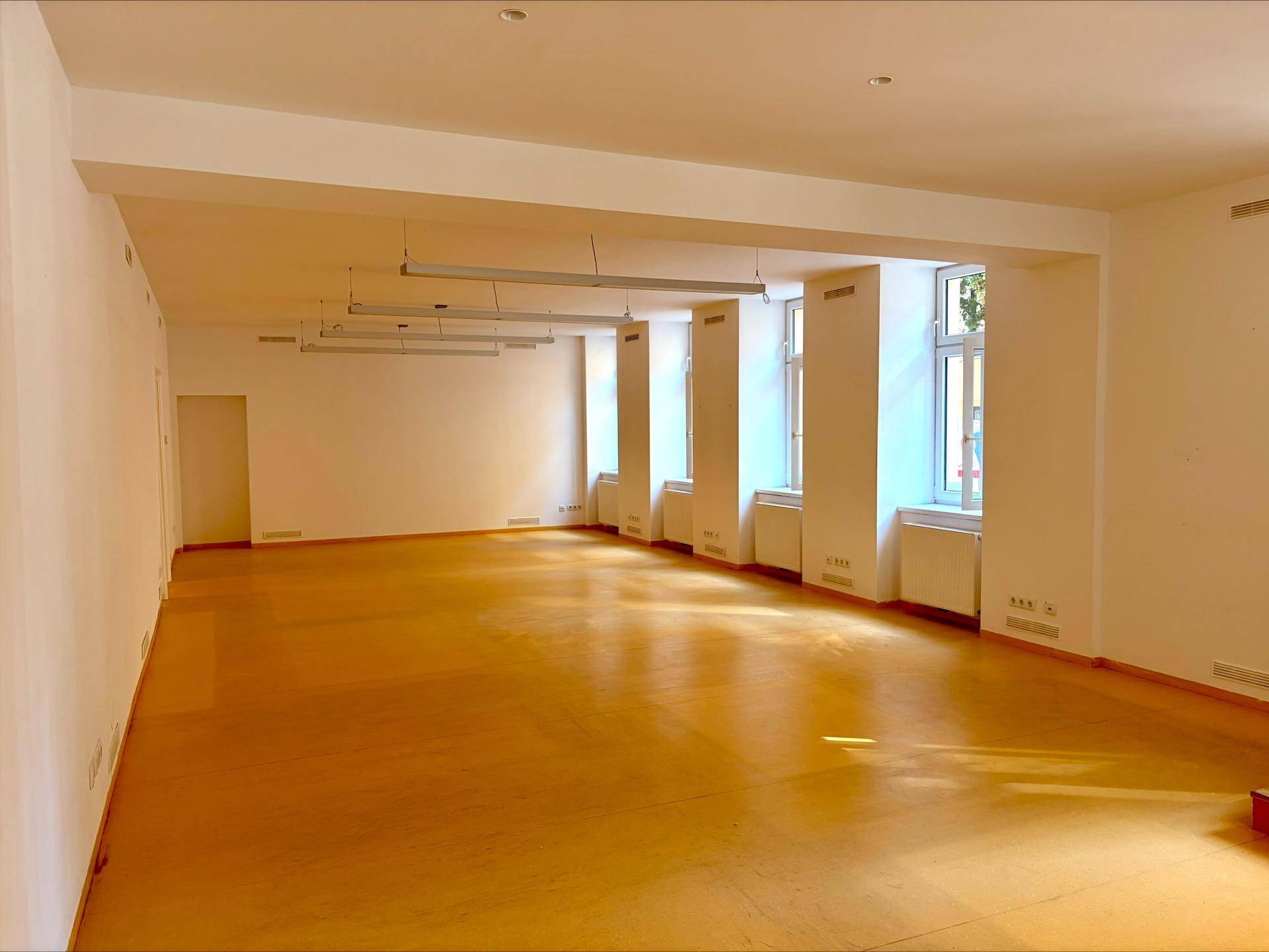 Langer, heller Büroraum mit zahlreichen Fenstern, die viel Tageslicht hereinlassen, und einem glänzenden Laminatboden.