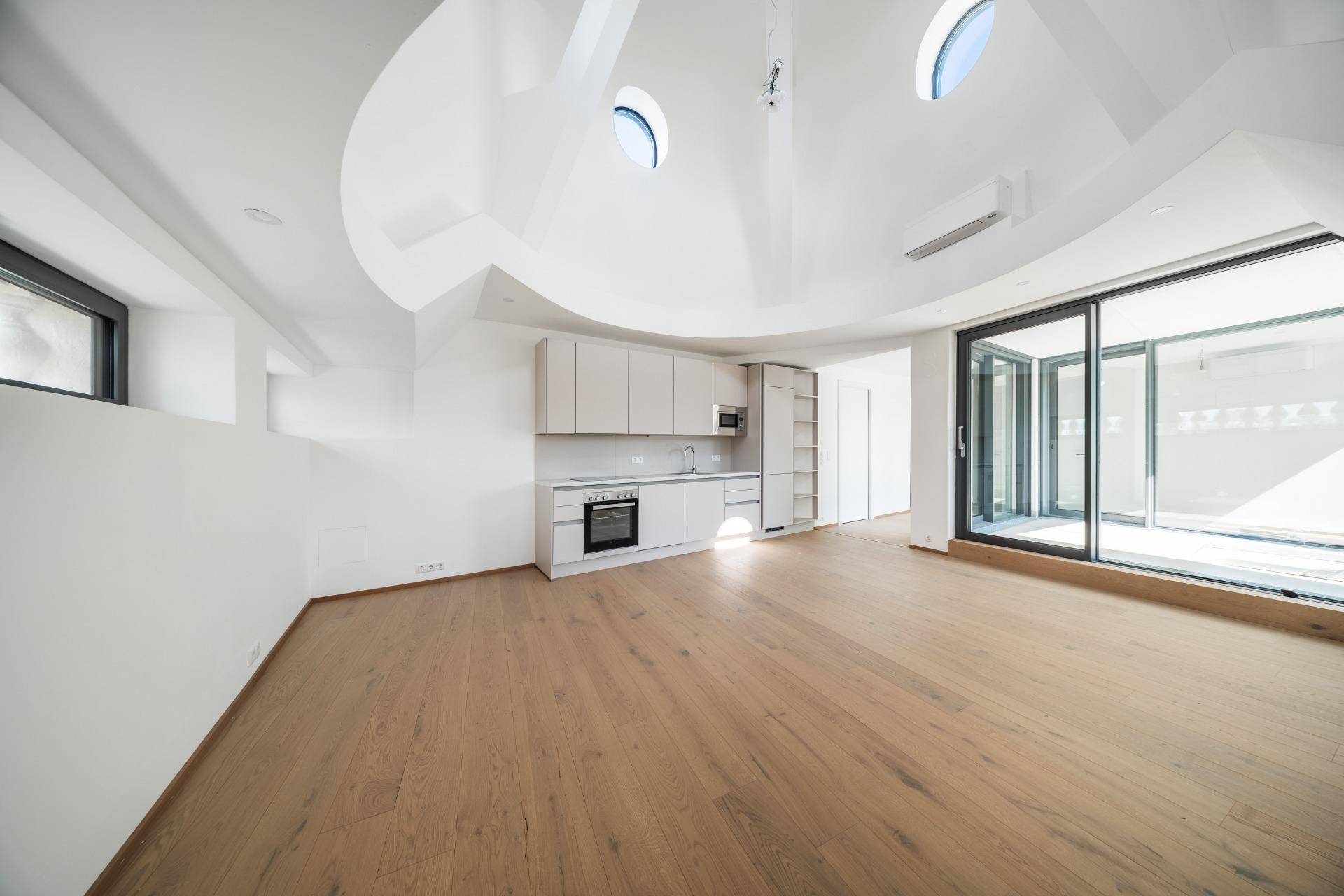 Geräumiger offener Wohnbereich mit integrierter Küchenzeile, Holzboden und Zugang zur Terrasse.