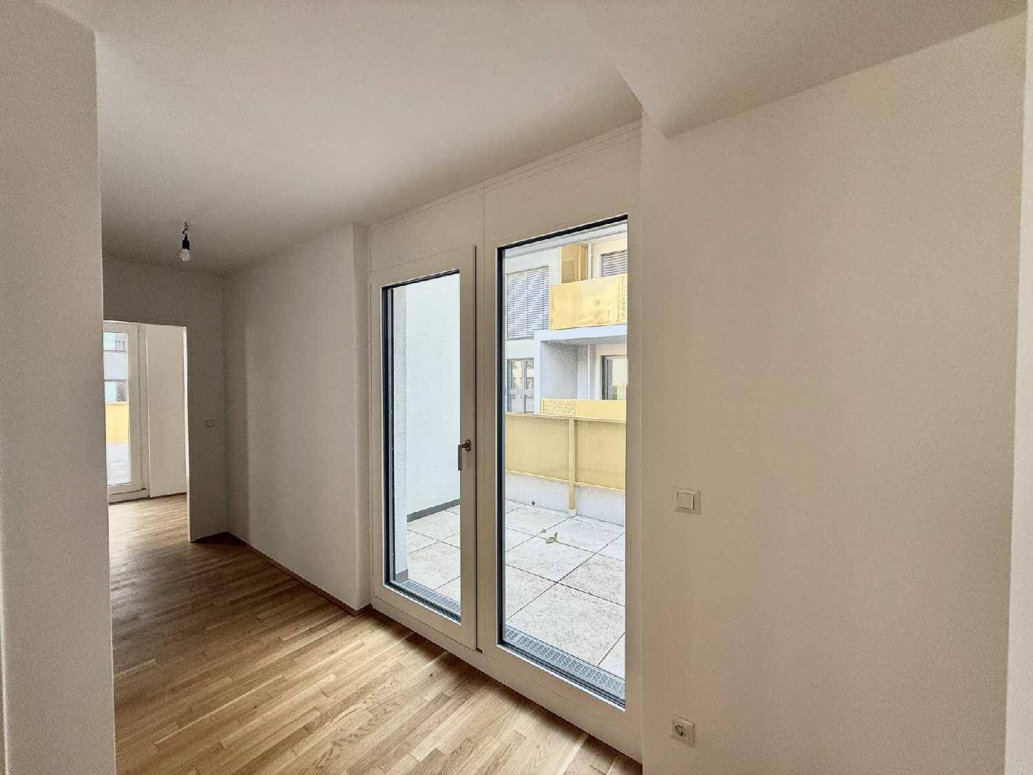 Geräumiger Wohnraum mit Holzboden und großen Glastüren, die auf eine Terrasse führen.