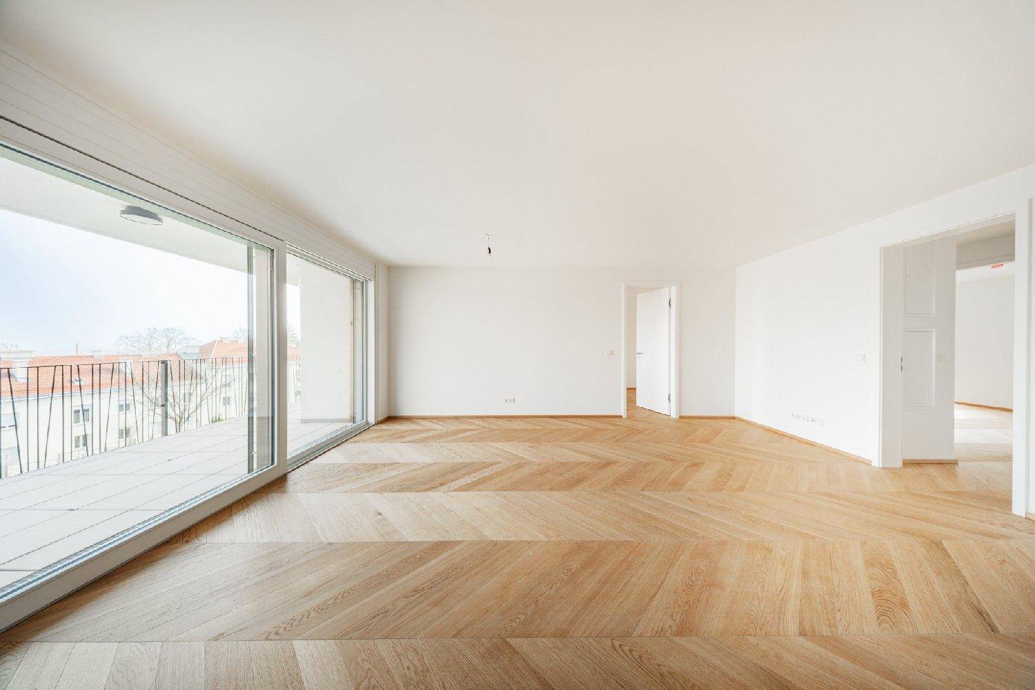 Geräumiger, heller Wohnbereich mit breiter Schiebetür zum großen Balkon und elegantem Parkettboden.