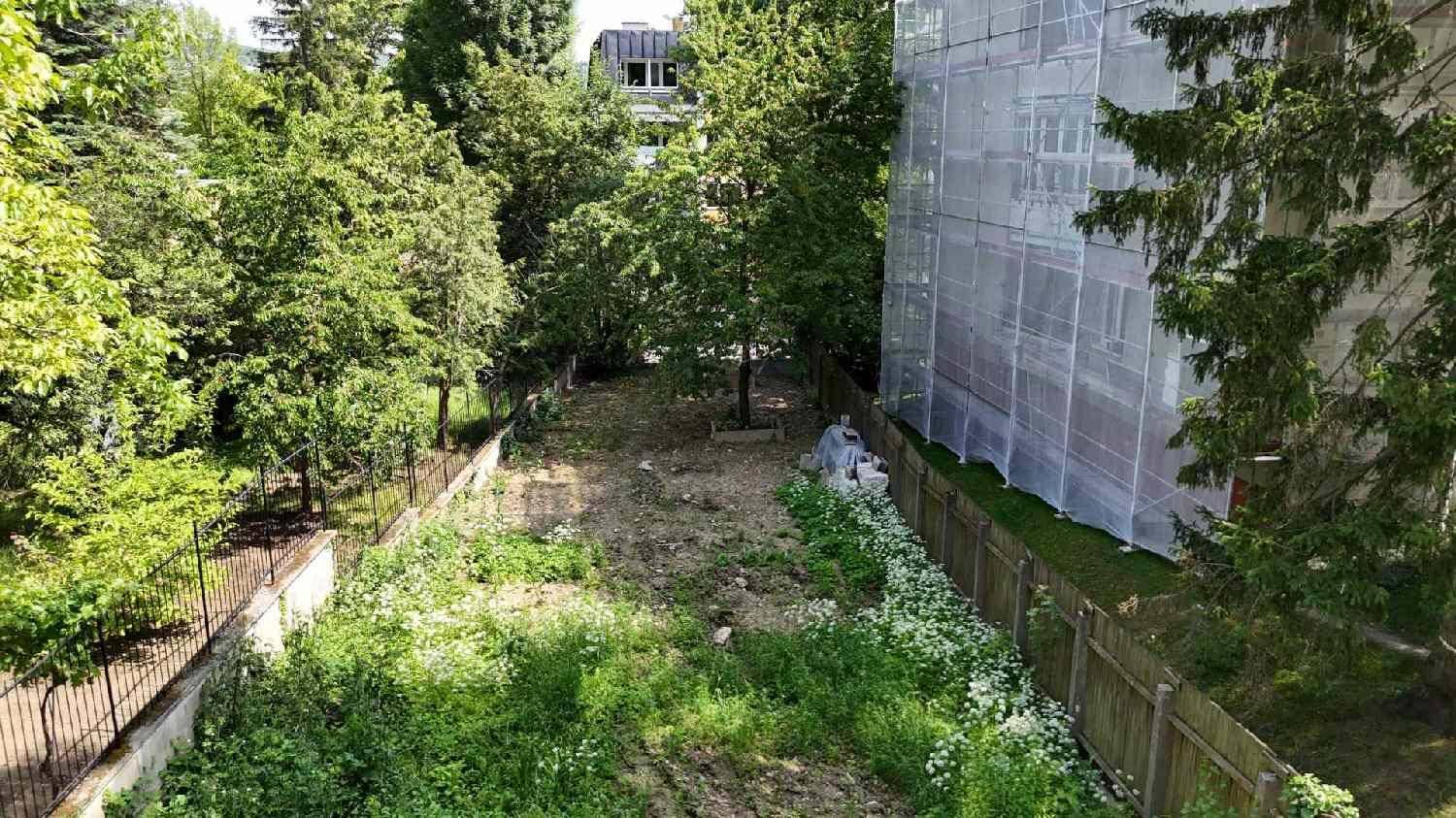 Unbebautes Grundstück mit viel Grün, umgeben von Zäunen und Bäumen, neben einem Gebäude.