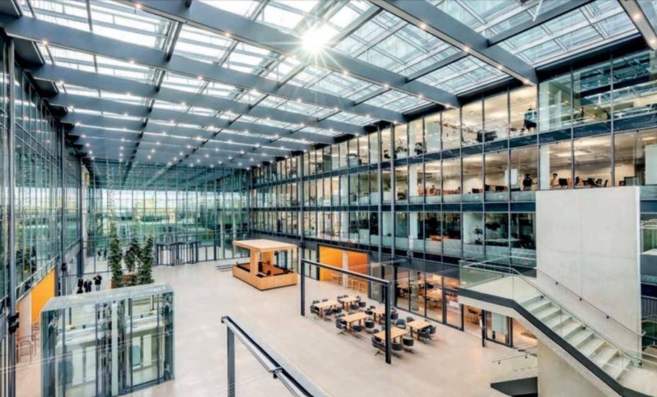 Großzügiges, modernes Büroatrium mit viel Tageslicht, Glasdach und mehreren Etagen, das eine offene und helle Atmosphäre schafft.