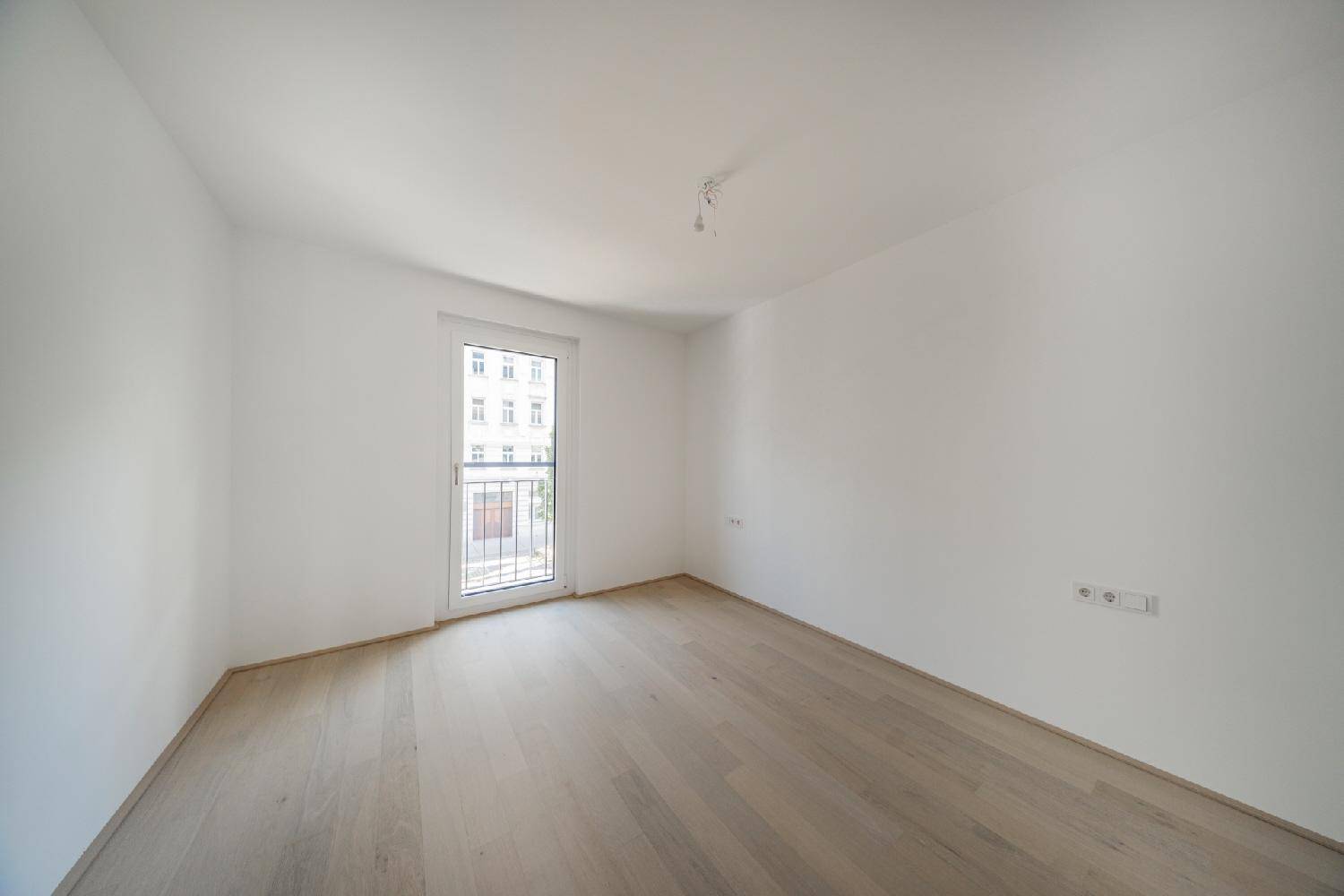 Geräumiges Zimmer mit Parkettboden und großem Fenster mit französischem Balkon.