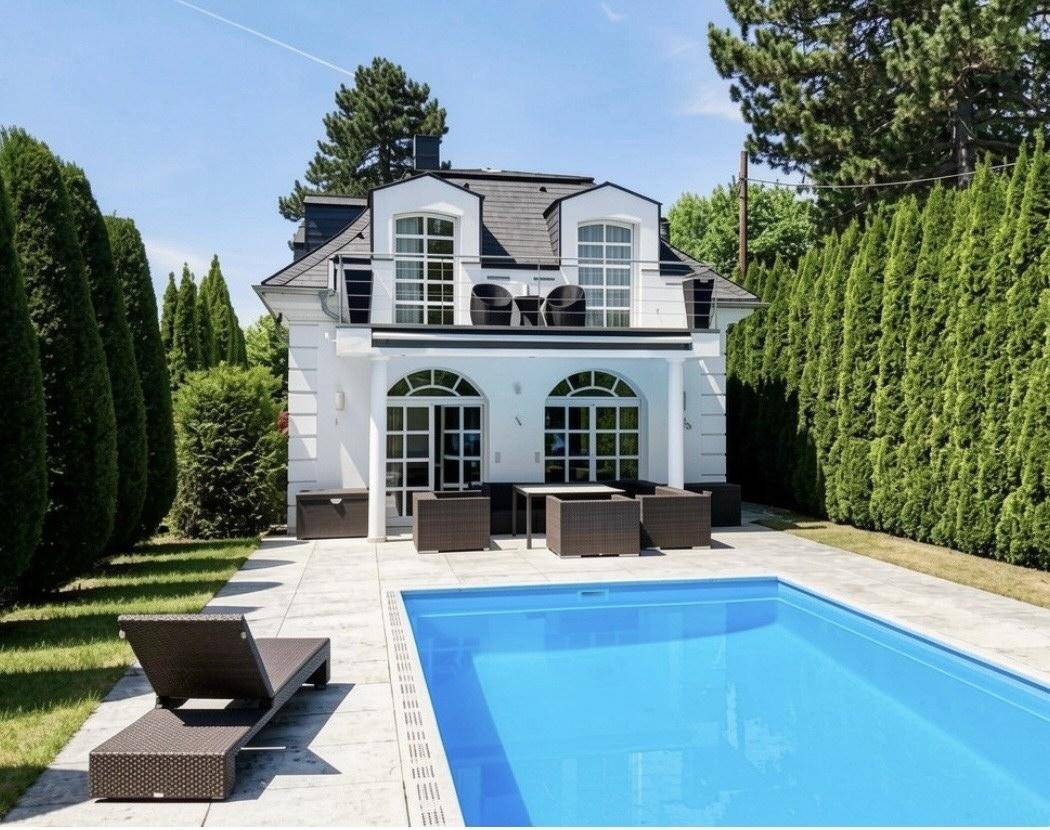 Exterieur der Stadtvilla mit Swimmingpool, gepflegtem Rasen und Hecken.