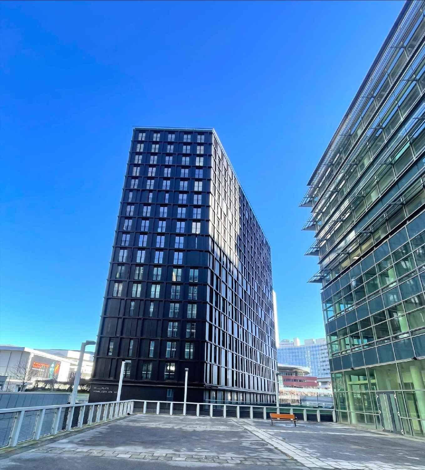 Schlankes, modernes Hochhaus mit dunkler Fassade und zahlreichen Fenstern, das sich gegen den klaren blauen Himmel abhebt.