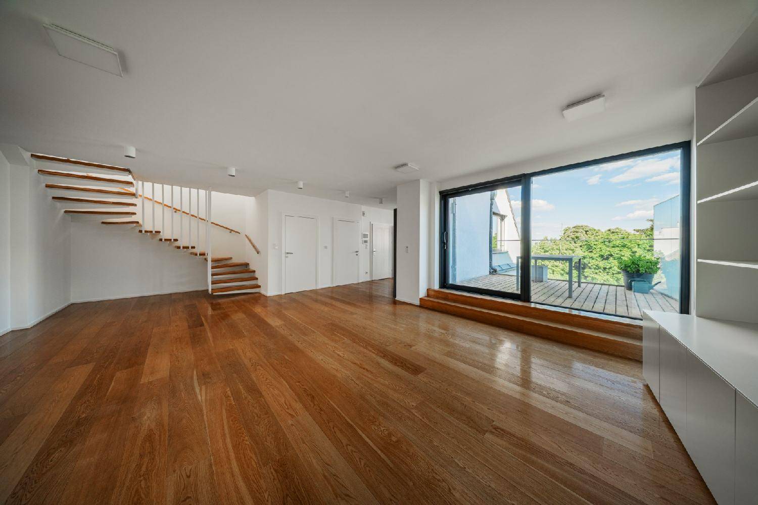 Geräumiger Wohnbereich mit Holzboden, offener Treppe und Zugang zu einer Außenterrasse.