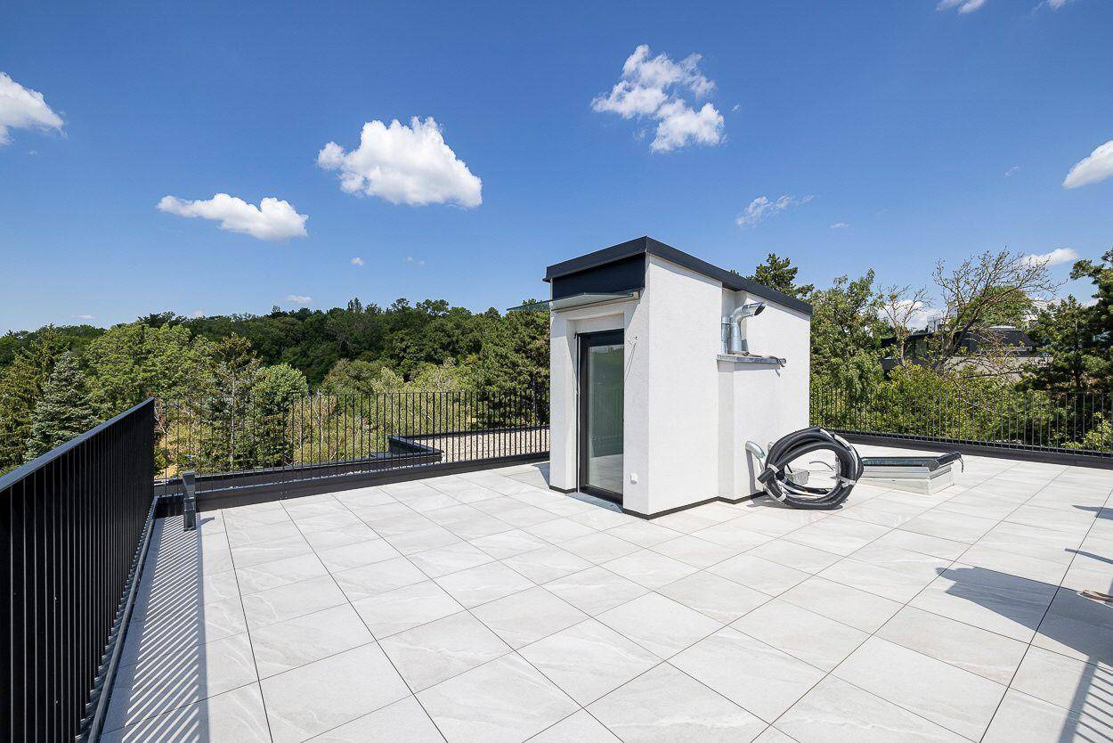Geräumige Dachterrasse mit hellem Fliesenboden und Blick auf die umliegenden Bäume.