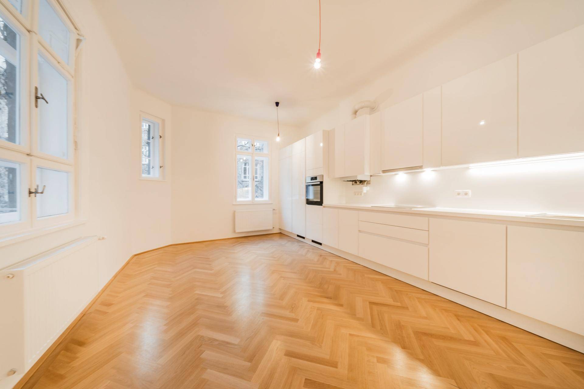 Moderne, helle Küche mit weißen Hochglanzfronten, integrierten Geräten und Fischgrätparkettboden.