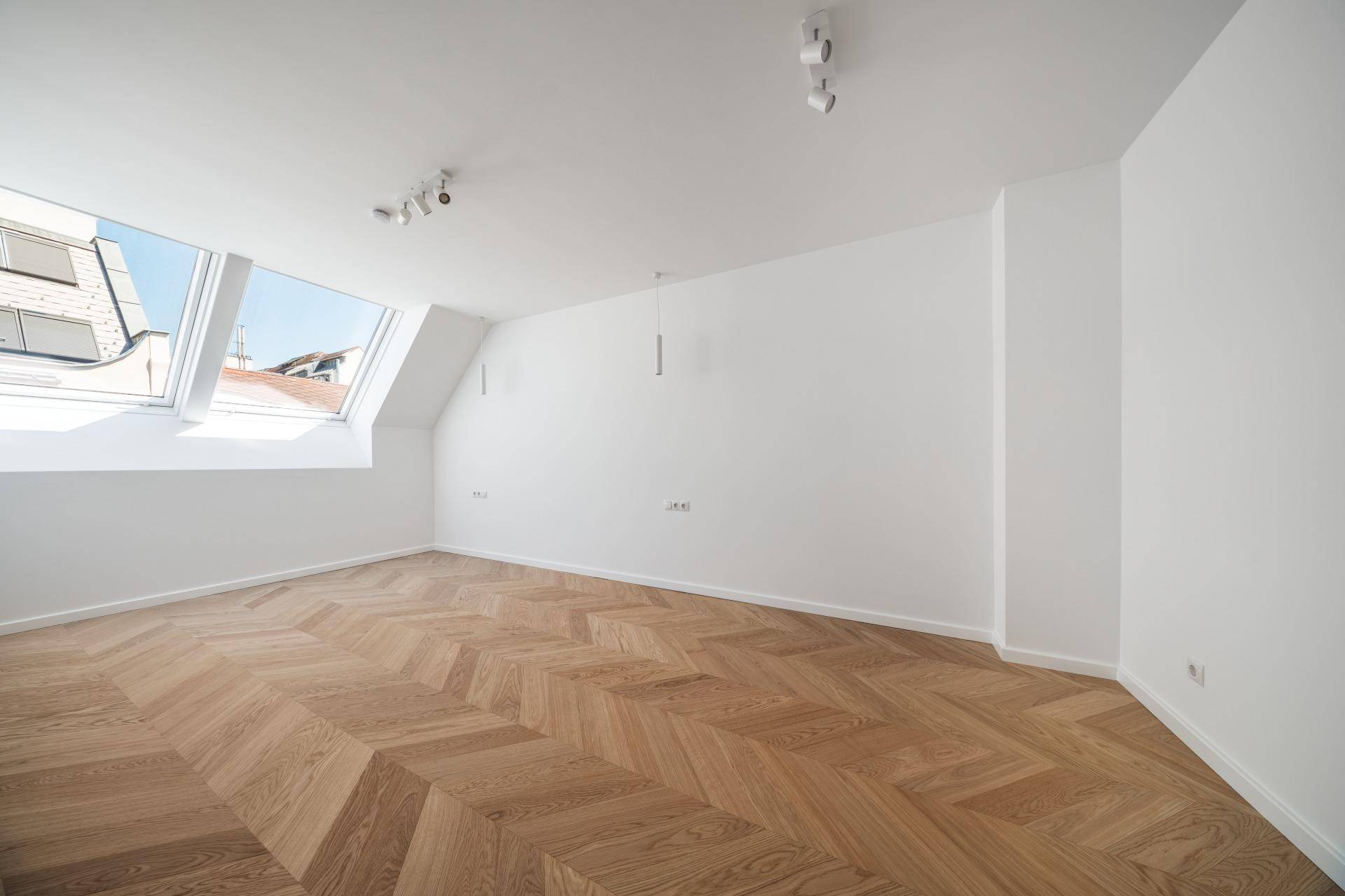 Ruhiges Zimmer im Dachgeschoss mit schrägen Wänden, Dachfenstern und hellem Fischgrätparkett.
