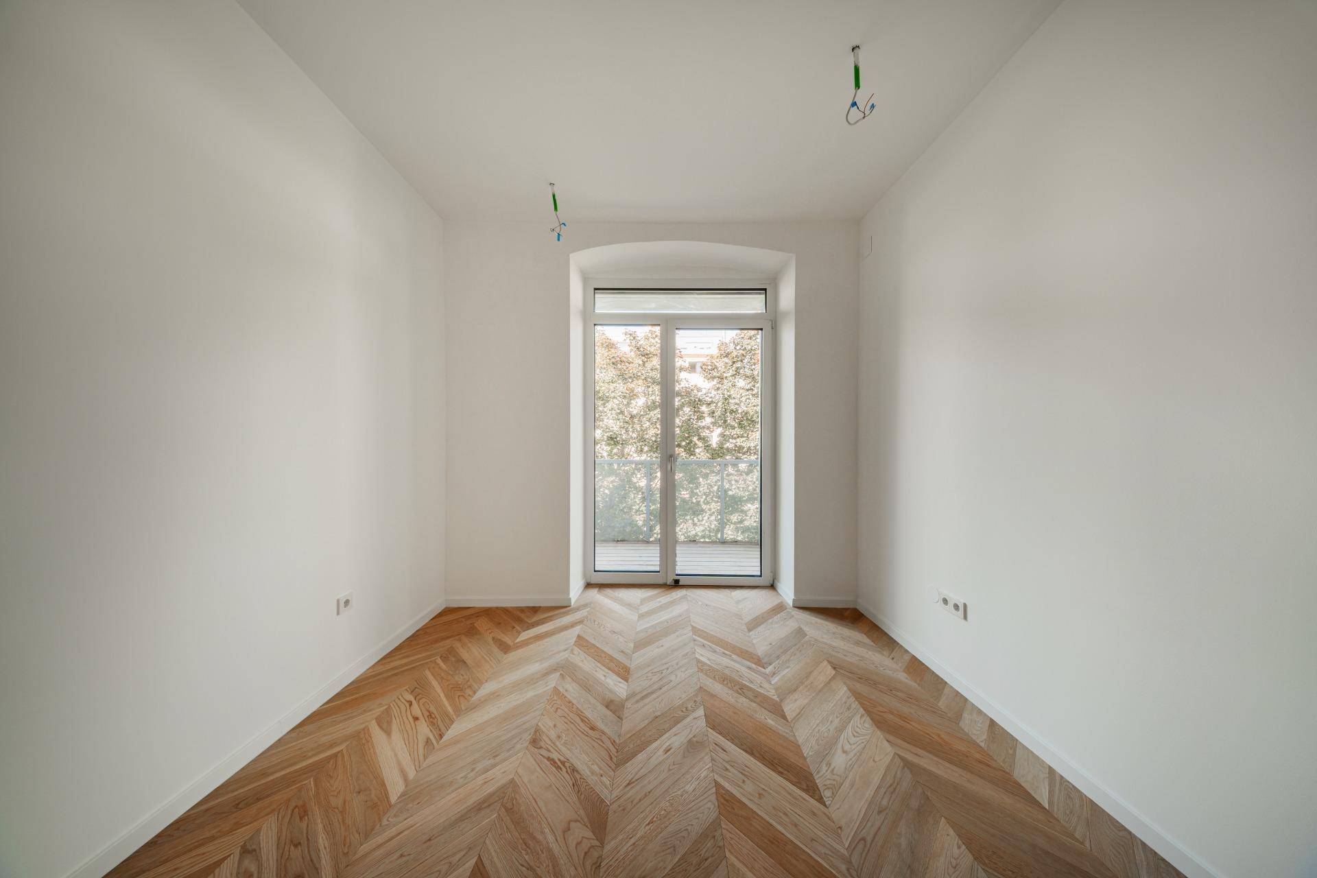Helles Zimmer mit Fischgrätparkett und einem großen Fenster, ideal als Schlaf- oder Arbeitszimmer.