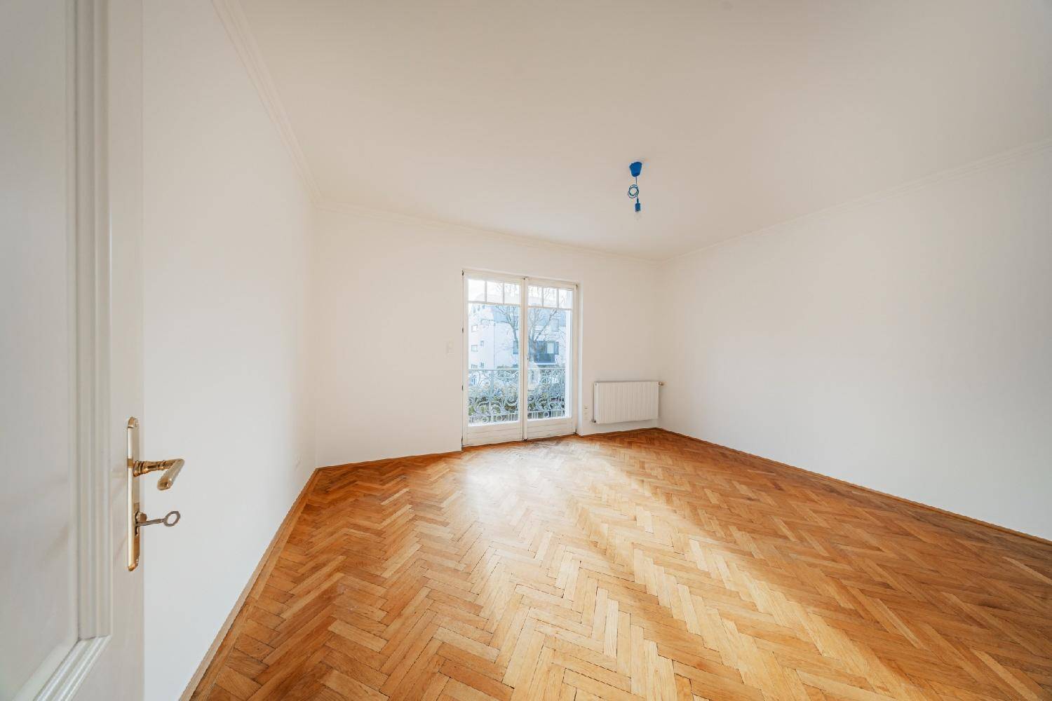 Helles Schlafzimmer mit Fischgrätparkett und Fenstertür zu einem französischen Balkon mit Ausblick.
